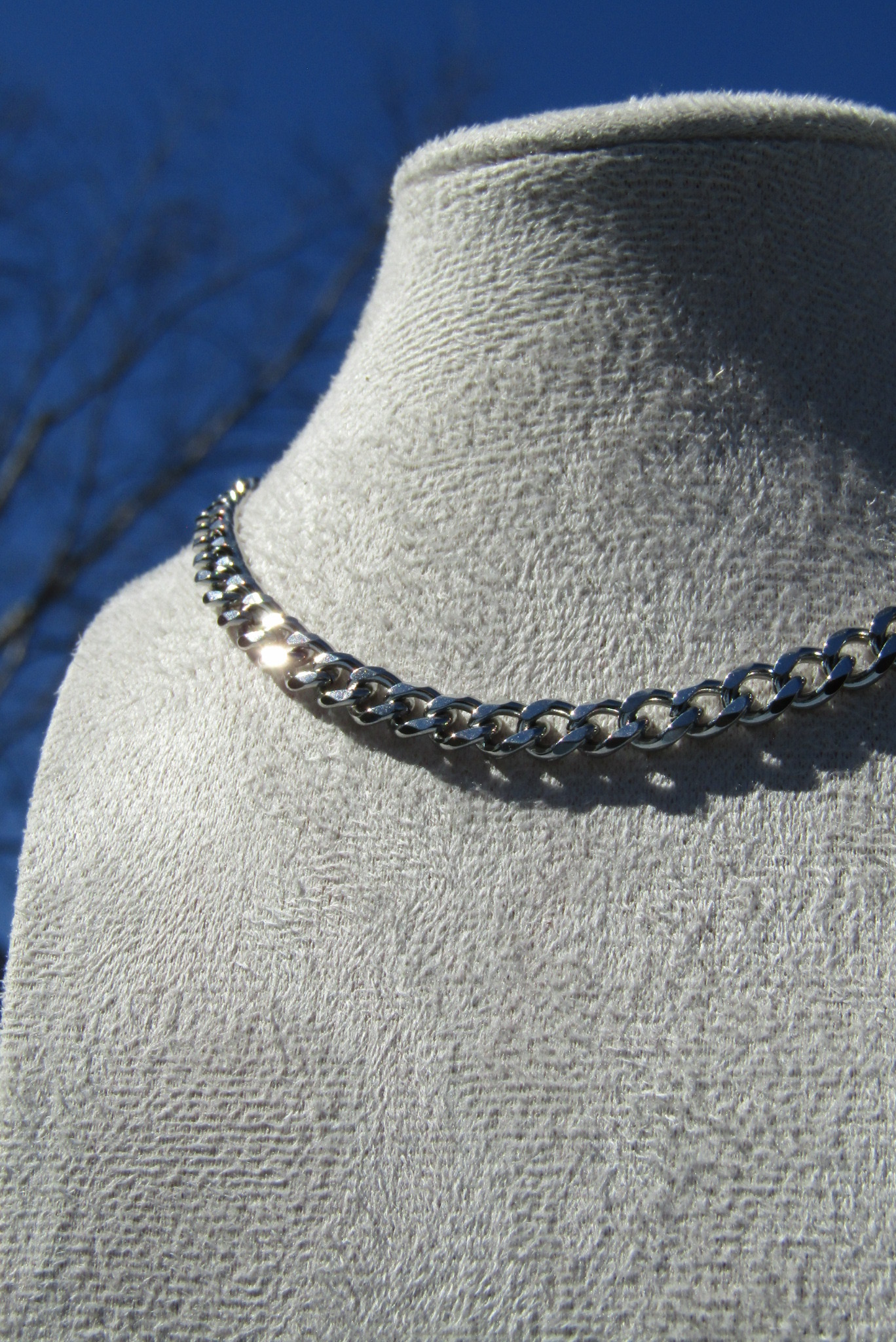 Silver chain necklace displayed on a light gray fabric surface with a blue background.