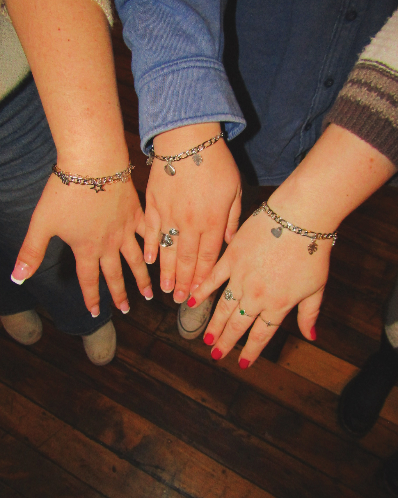 Three hands with jewelry, including bracelets and rings, resting on a wooden floor.
