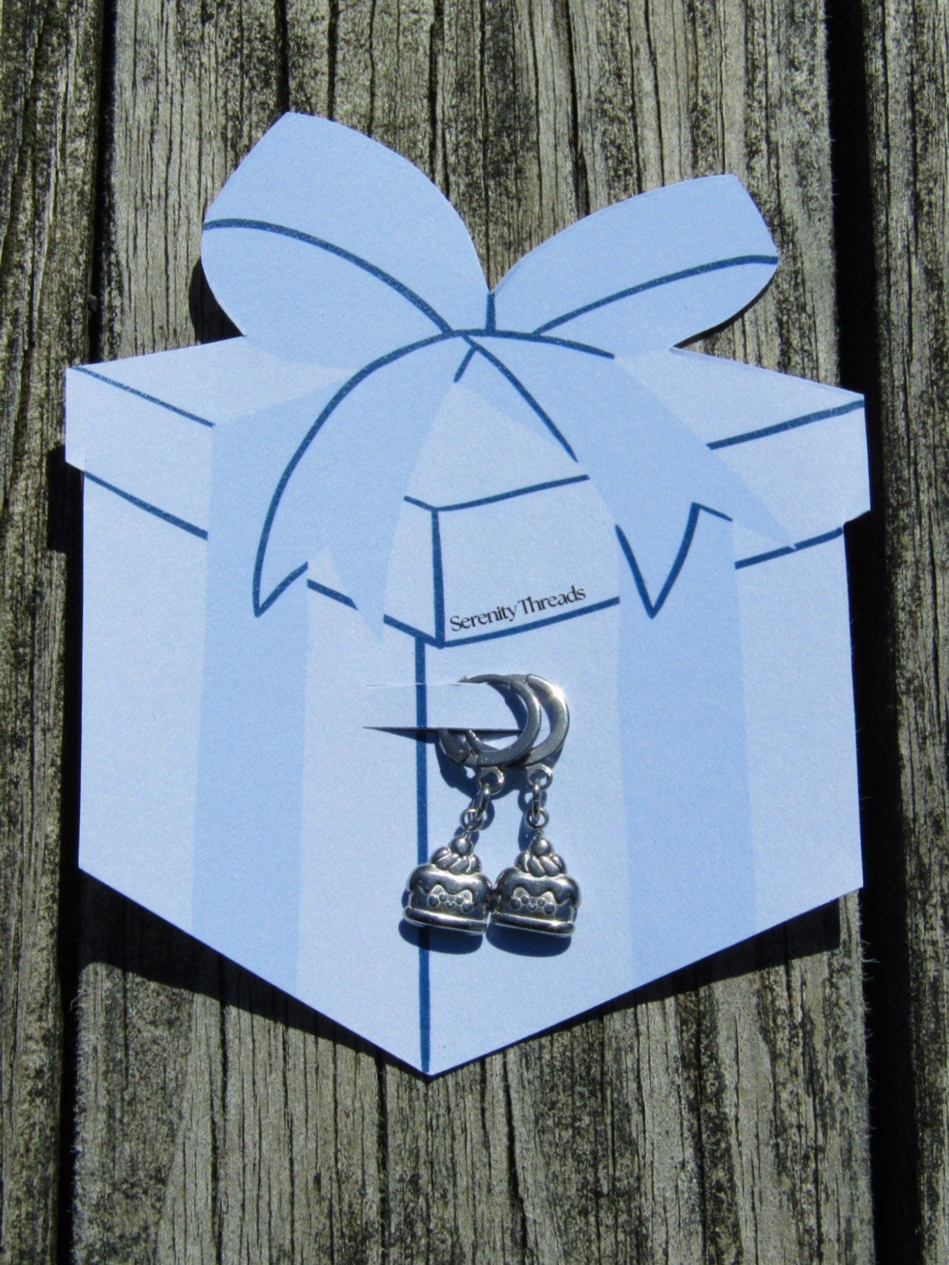 Blue paper gift box with a bow on top, hanging on a wooden surface, with a small silver charm attached.