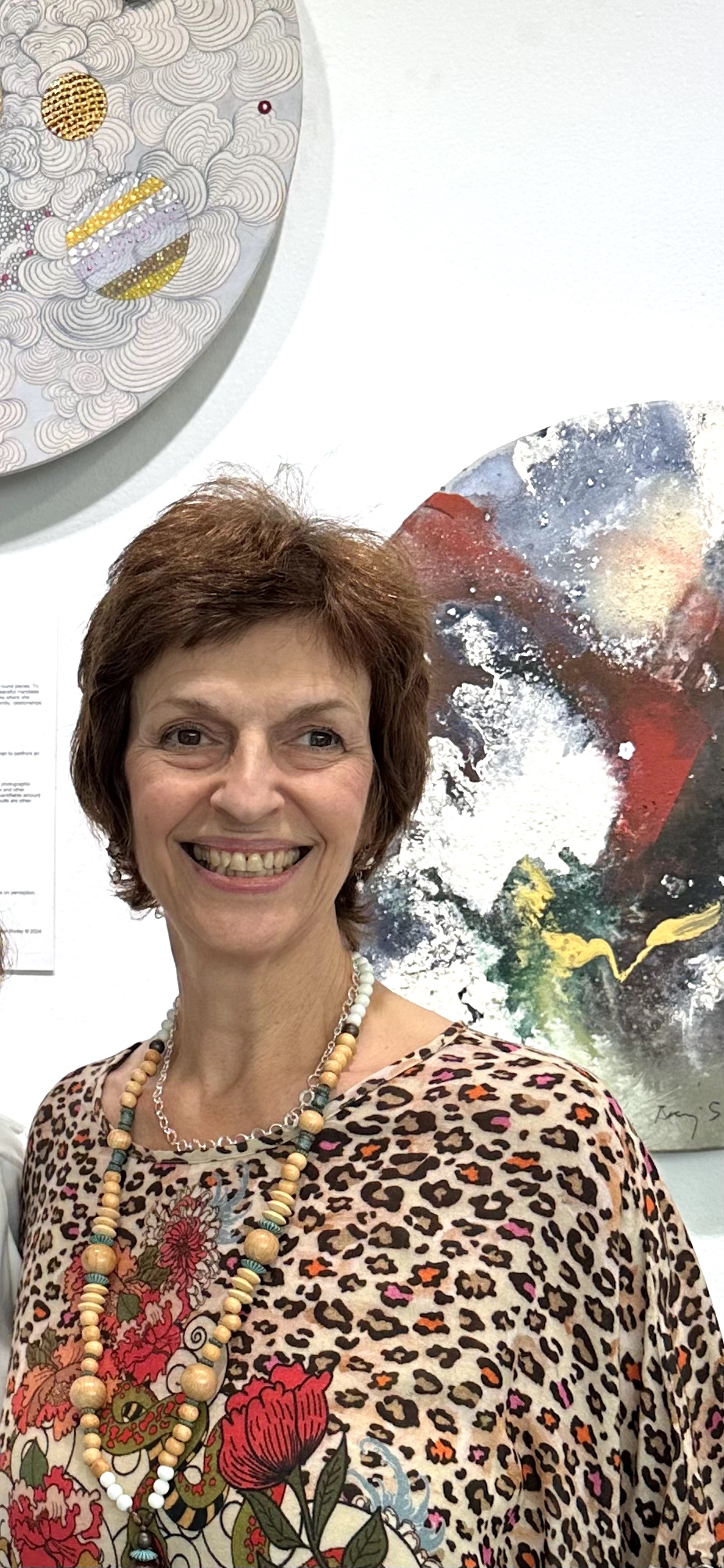 Smiling woman with short brown hair wearing a leopard print top and colorful necklace.