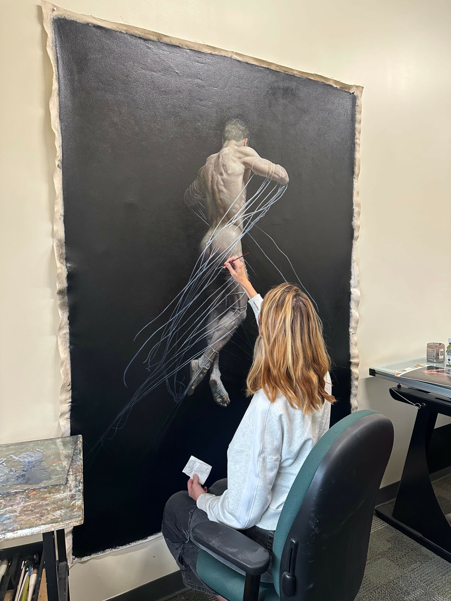 Person with long hair and white shirt interacts with a hanging art installation in a room.
