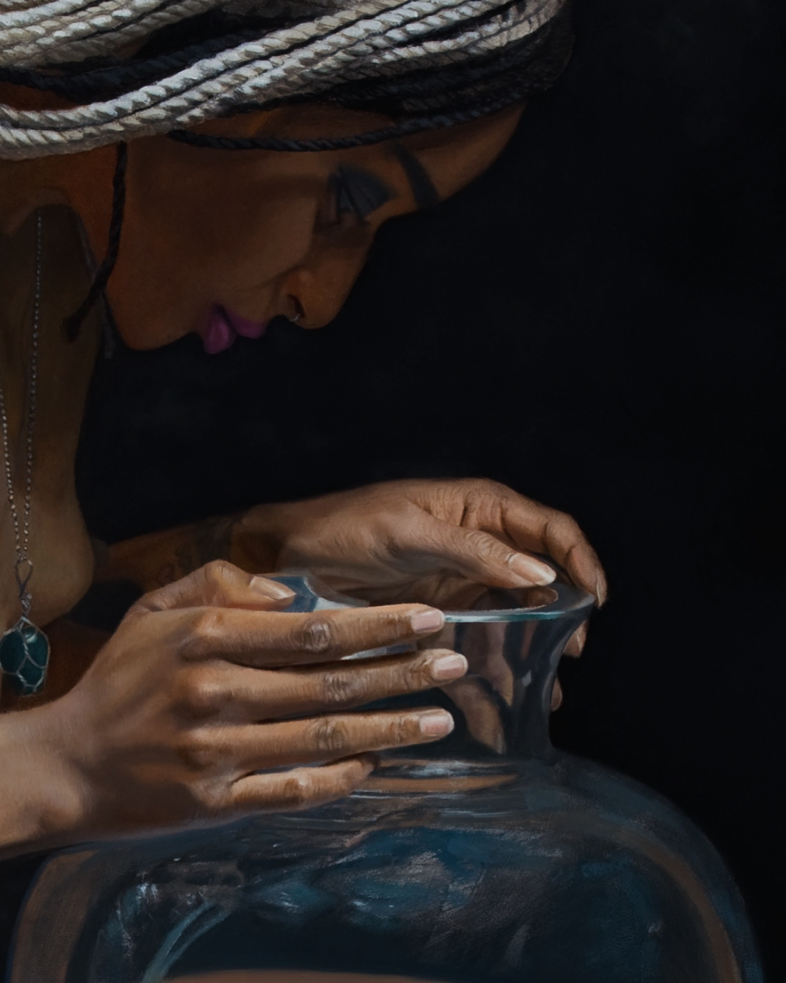 Person with braided hair and glasses holding a reflective object, focused on it, with a dark background.