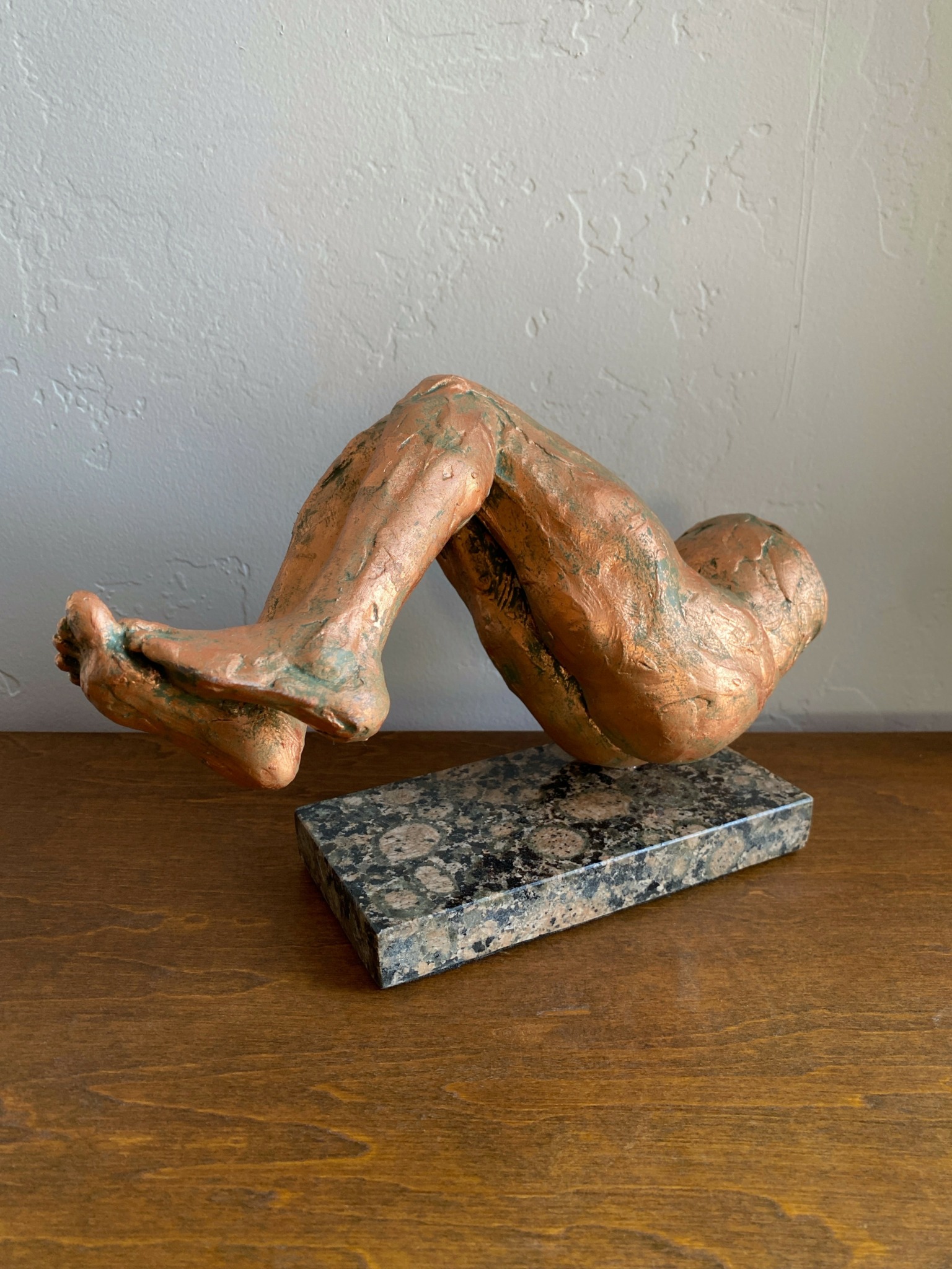 Sculpture of a human figure lying on a rectangular stone base, with legs bent and arms crossed over chest.