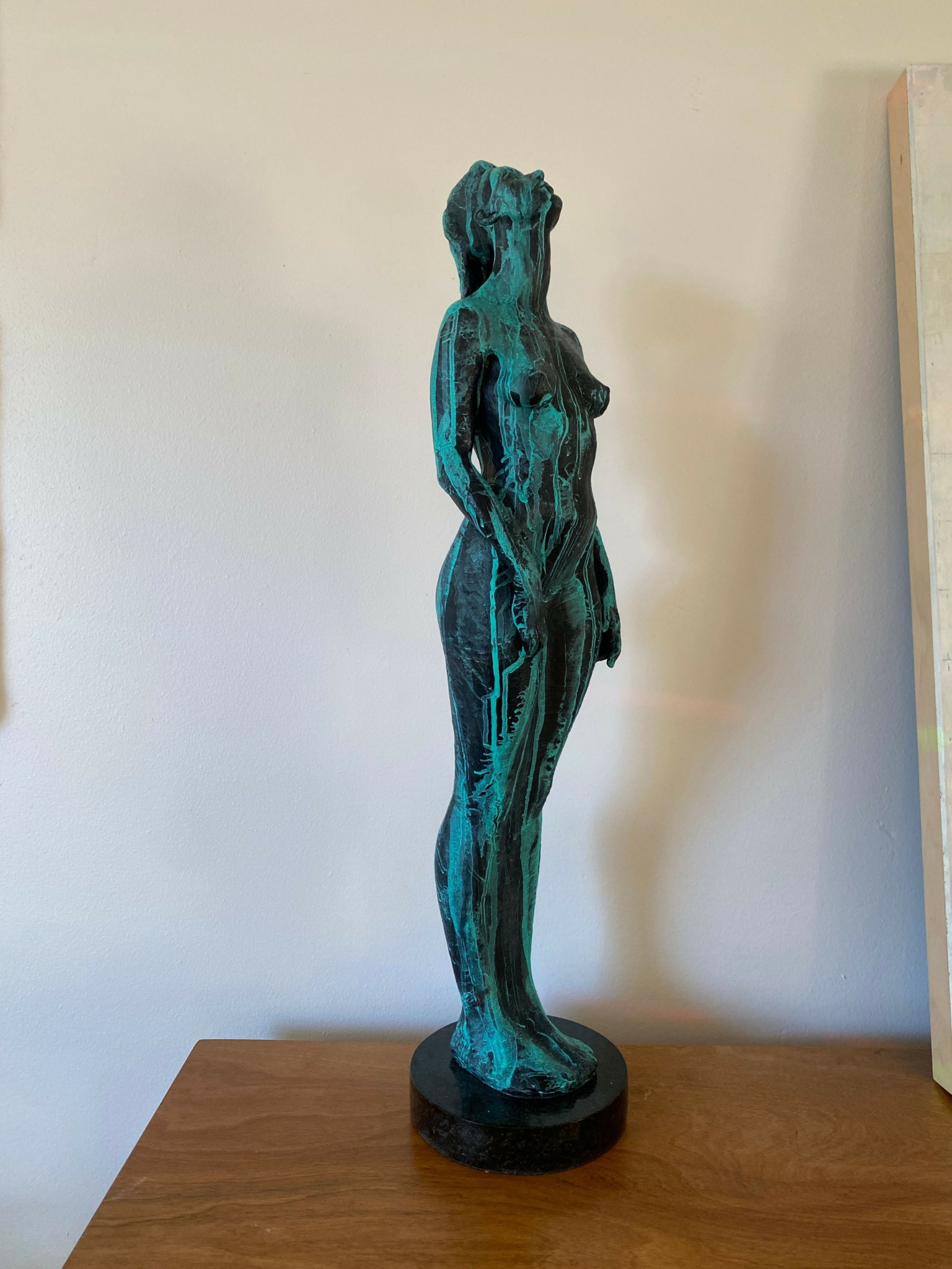 Bronze sculpture of a standing woman with flowing hair and draped clothing, mounted on a round base.
