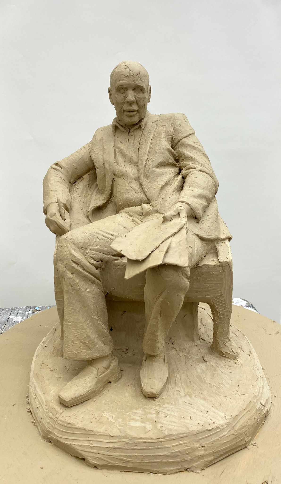 Sand sculpture of a seated man in a suit with crossed legs and one arm resting on the chair.