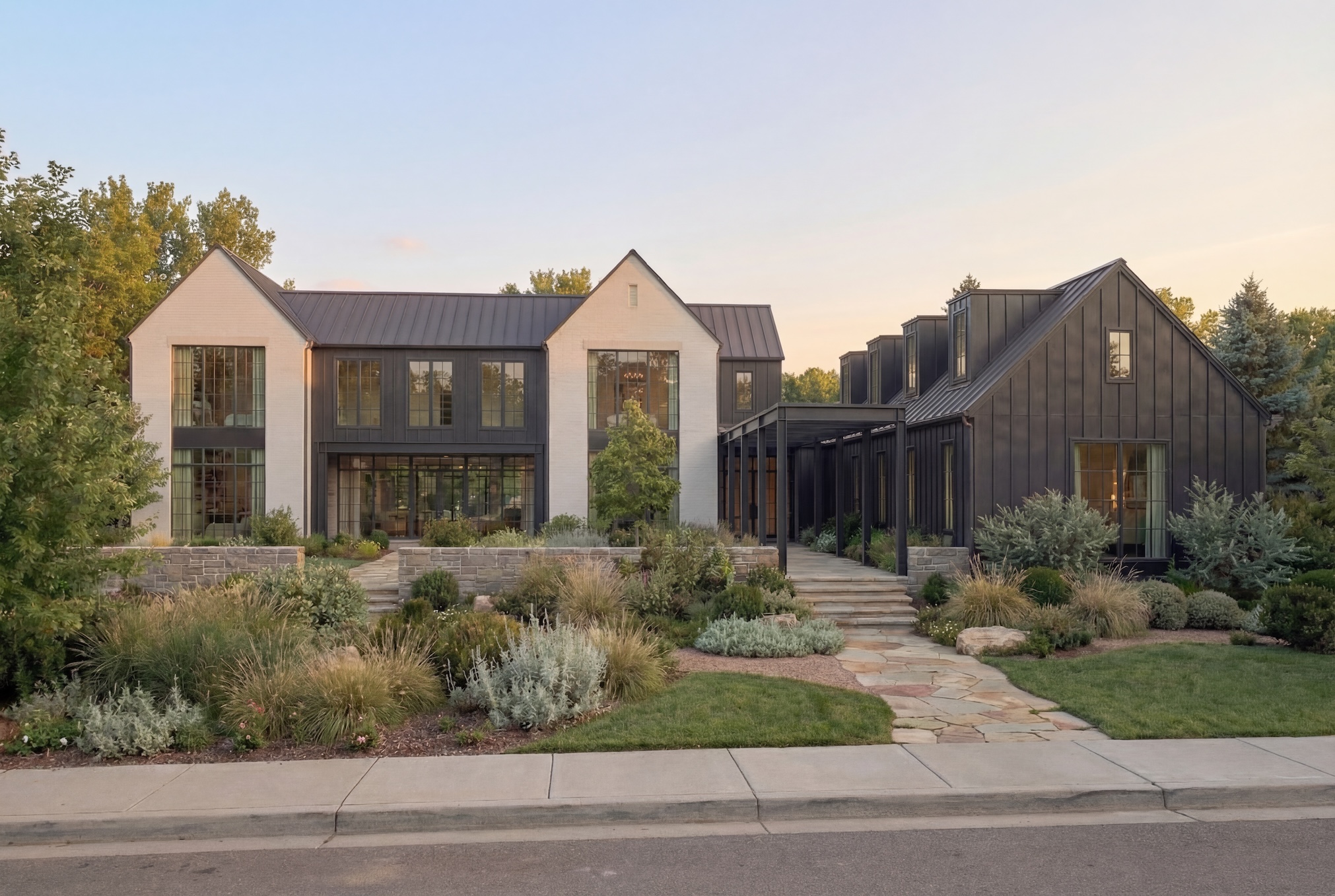 Modern two-story house with white and dark exterior, surrounded by landscaped garden and pathway, under a clear sky.