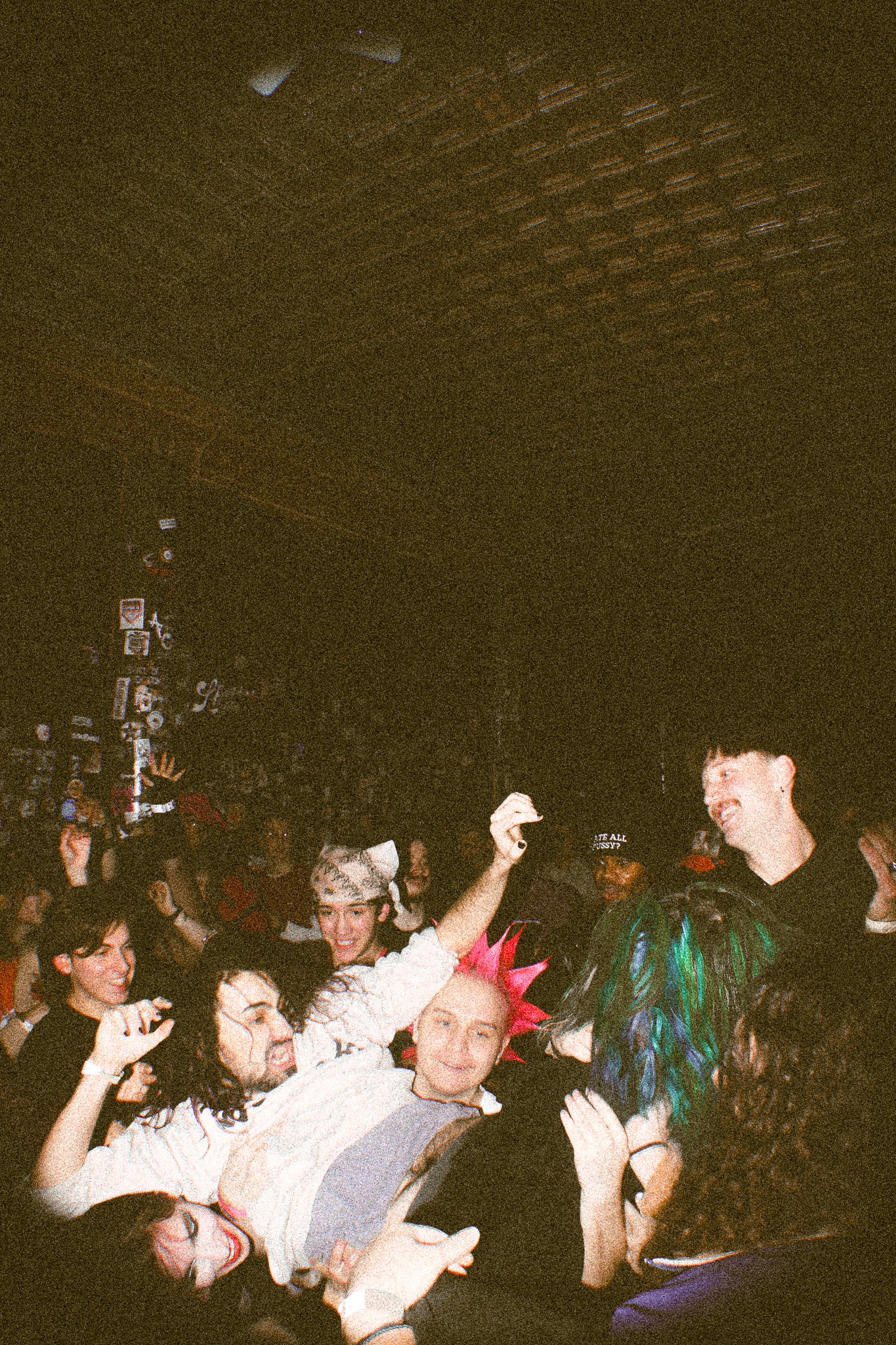 Group of people at a party or event, some wearing costumes or accessories, in a dimly lit indoor space.