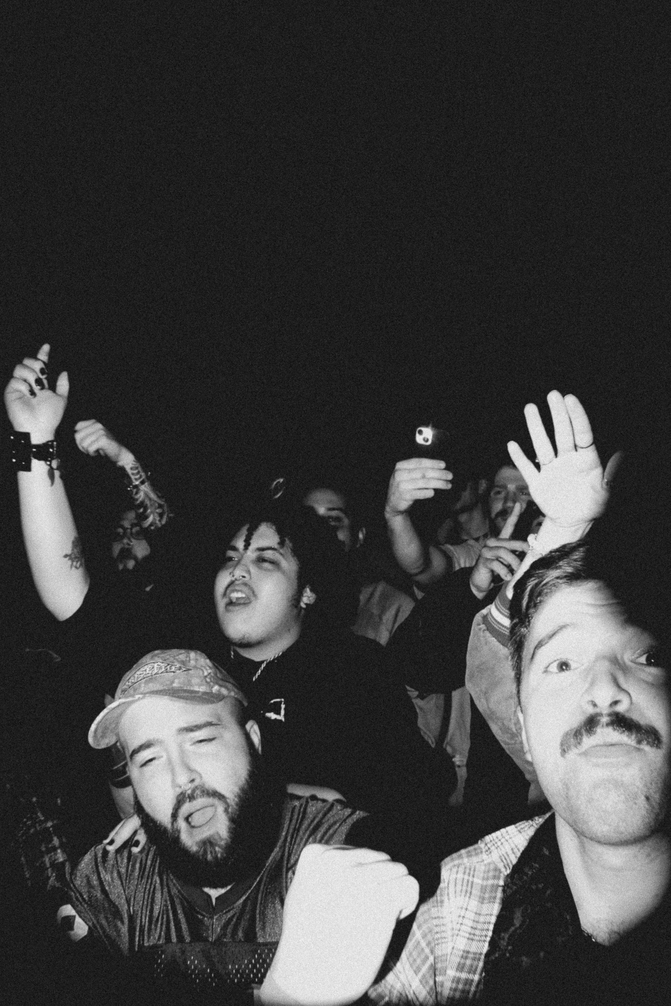 Group of people at a concert or event, some with hands raised, in black and white.