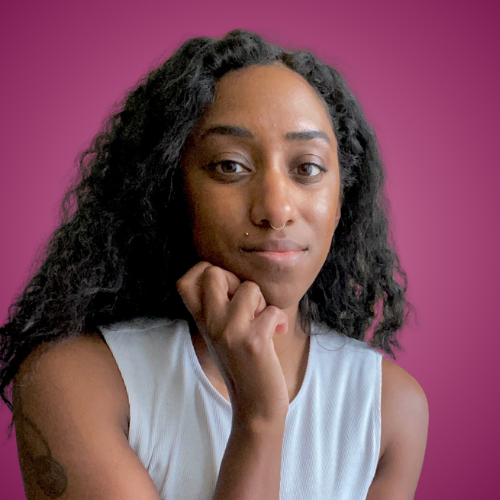 Young woman with curly hair resting her chin on her hand against a pink background.
