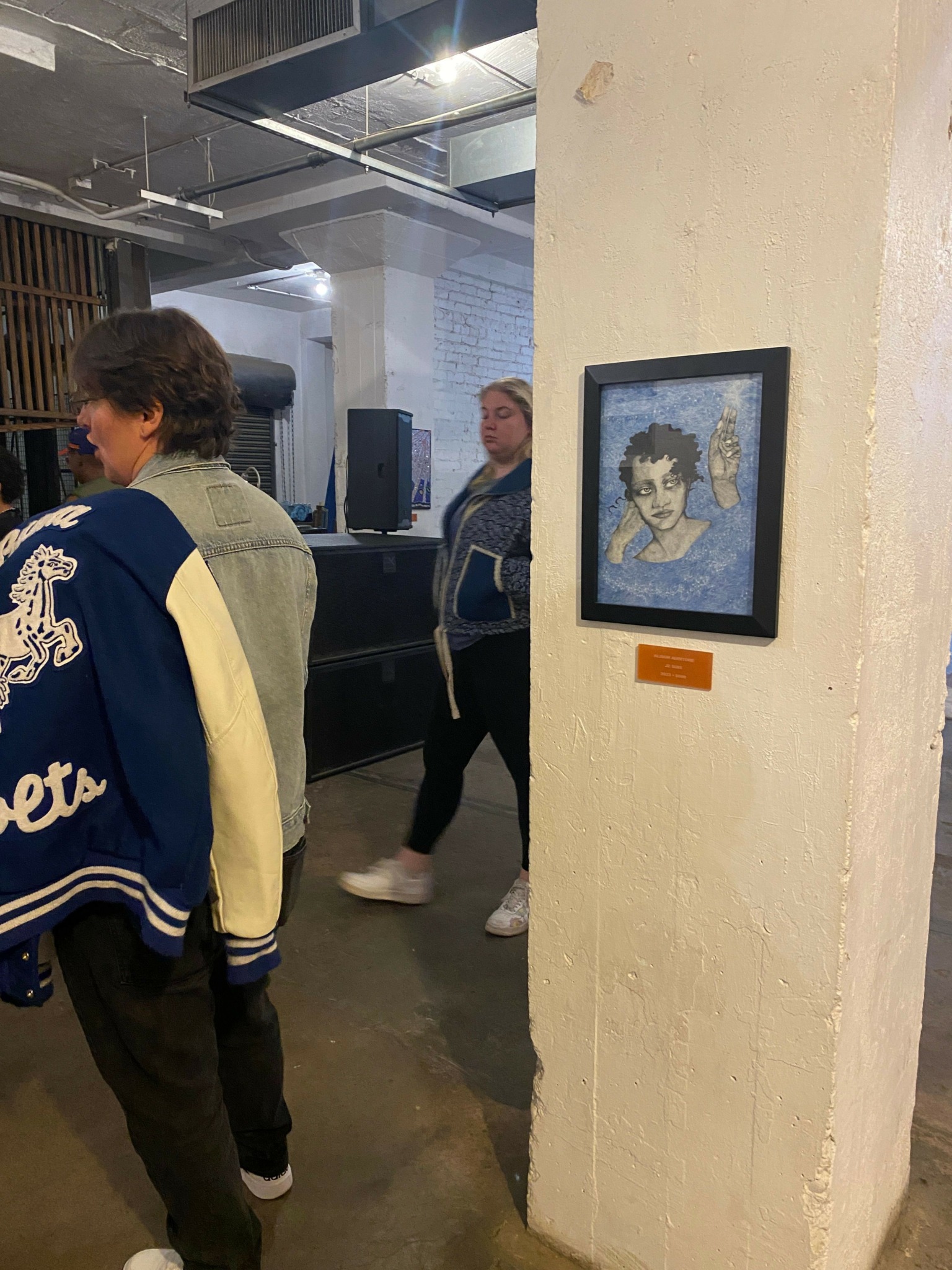 Two people walking in an indoor space with a framed picture on the wall behind them.