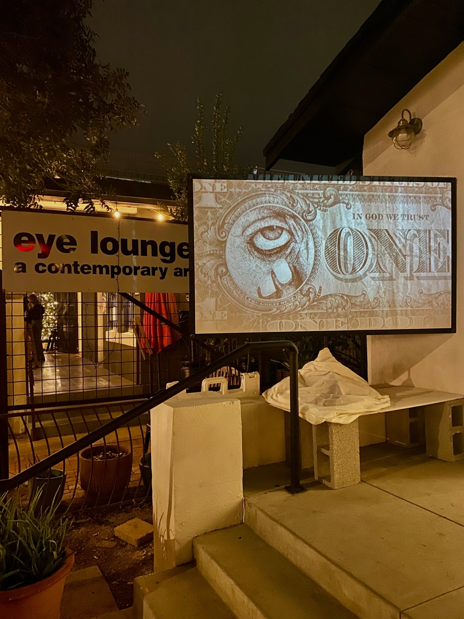 Projection screen displaying an eye illustration outside at night, with a sign reading 'eye lounge' nearby.
