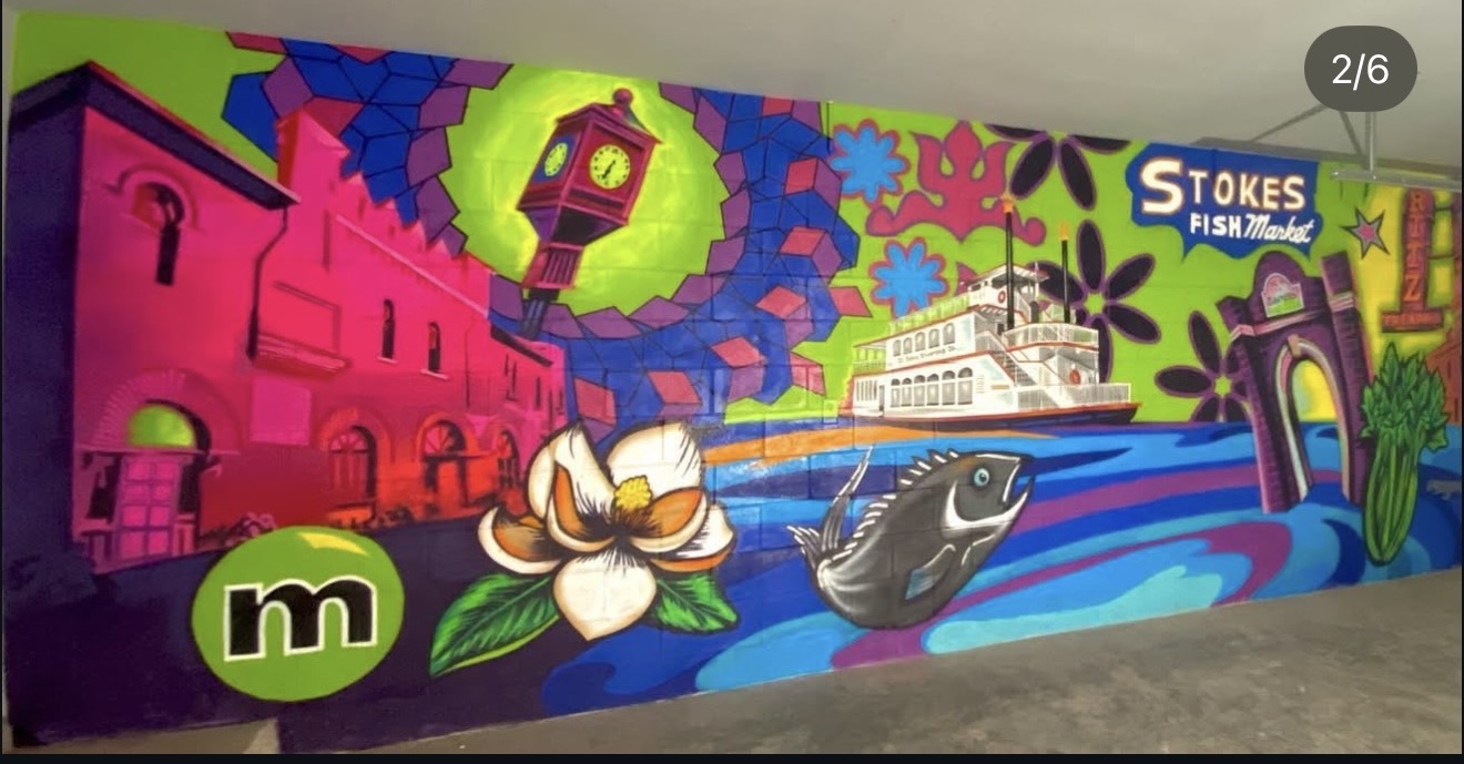 Colorful mural with a ship, whale, flowers, and abstract shapes on a wall.