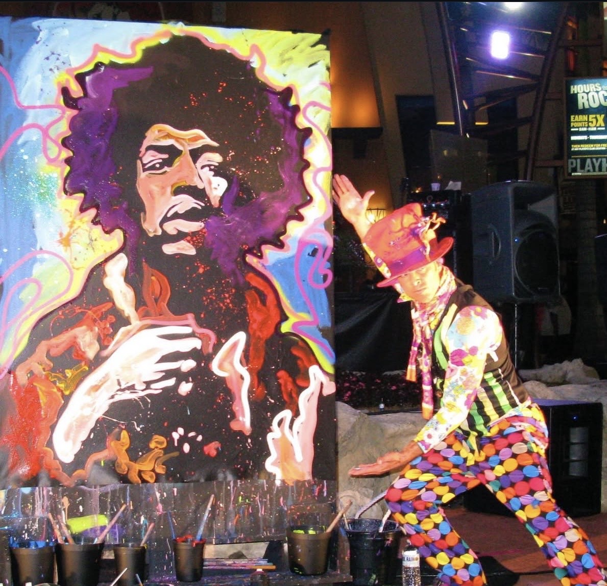 Colorful painting of a person with curly hair and a beard, next to a performer in a multicolored costume.