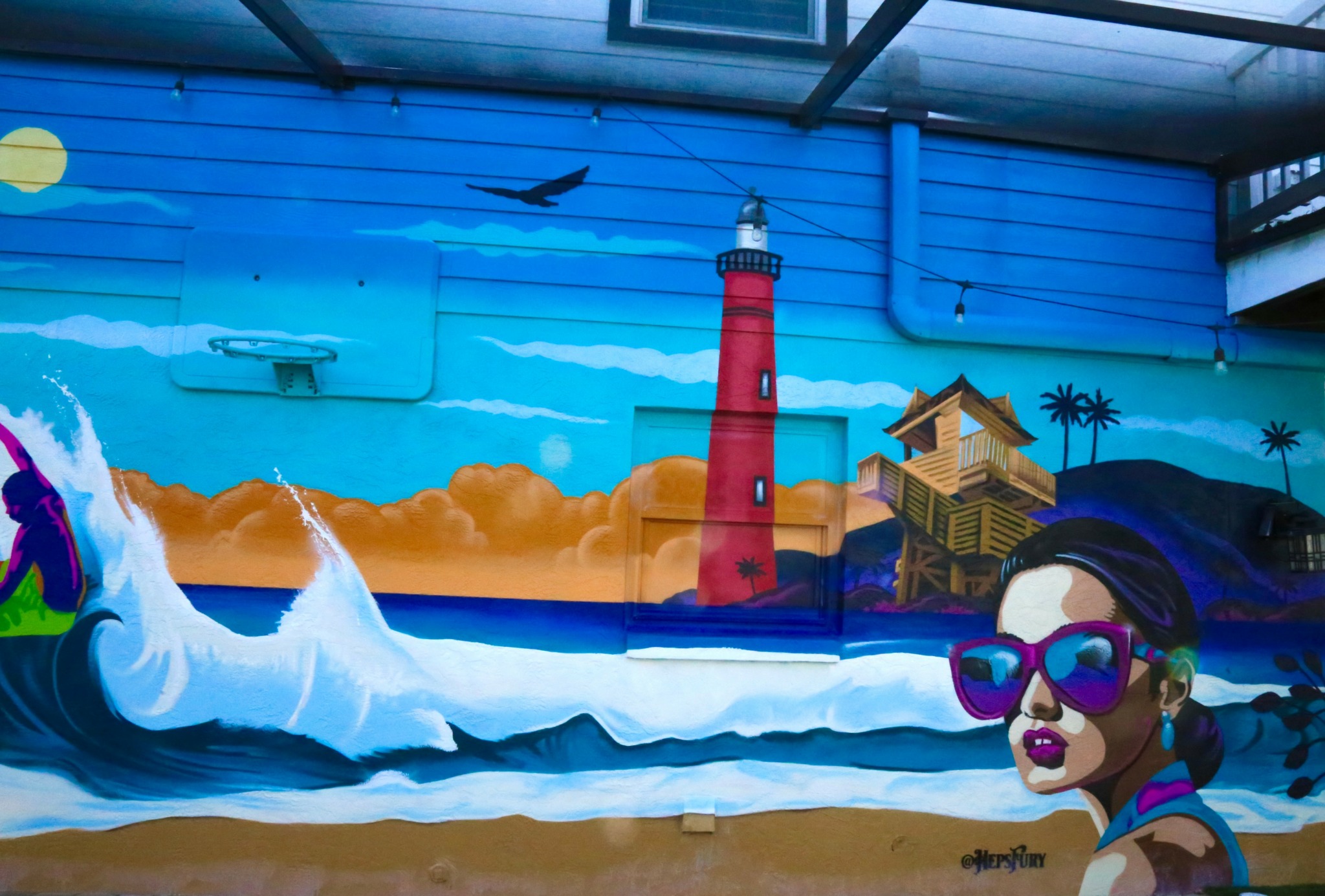Colorful mural of a lighthouse, waves, and a woman with sunglasses on a beach scene.