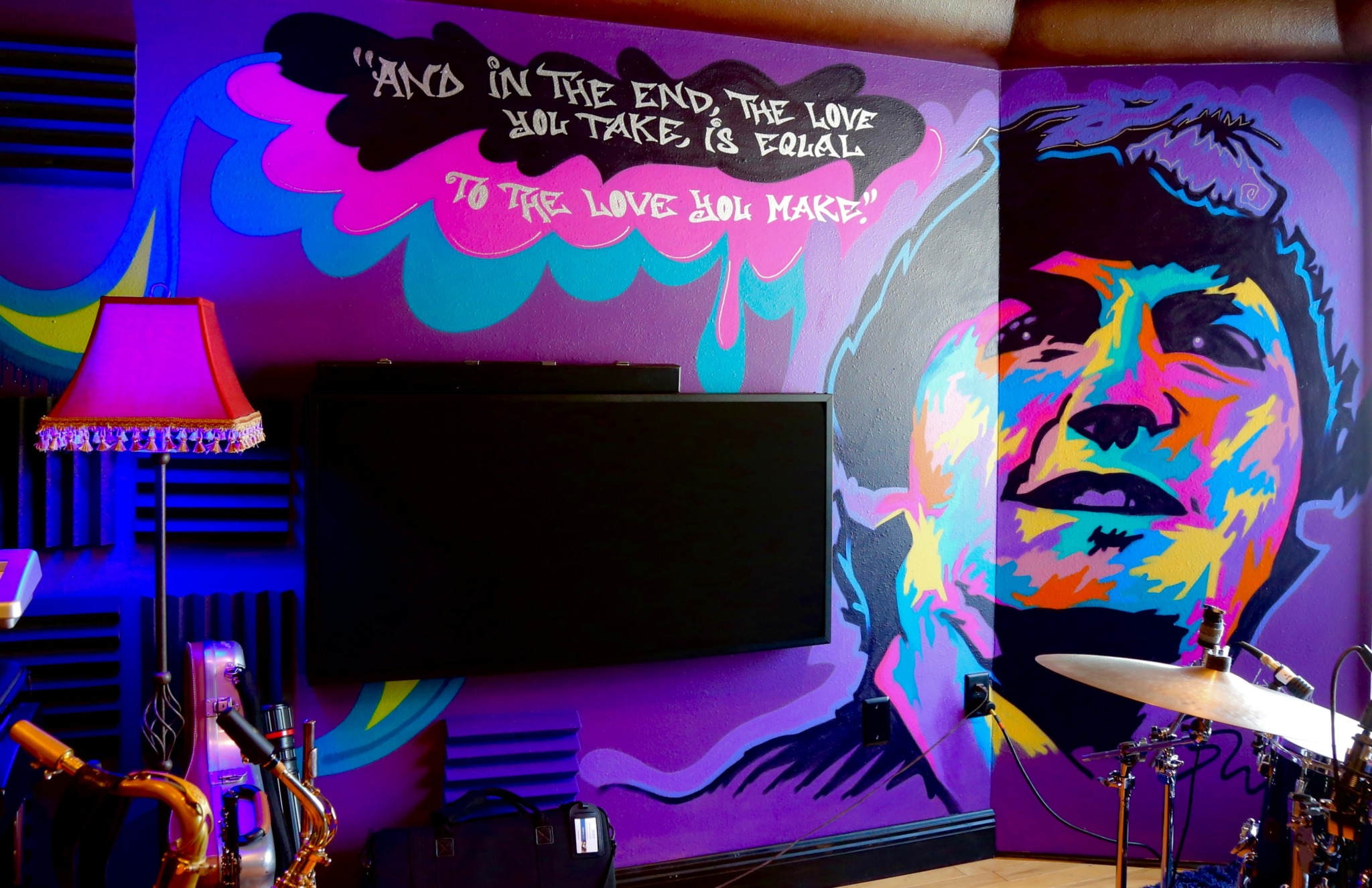 Colorful mural of a woman's face with vibrant paint strokes, a TV, and a pink lamp in a room.