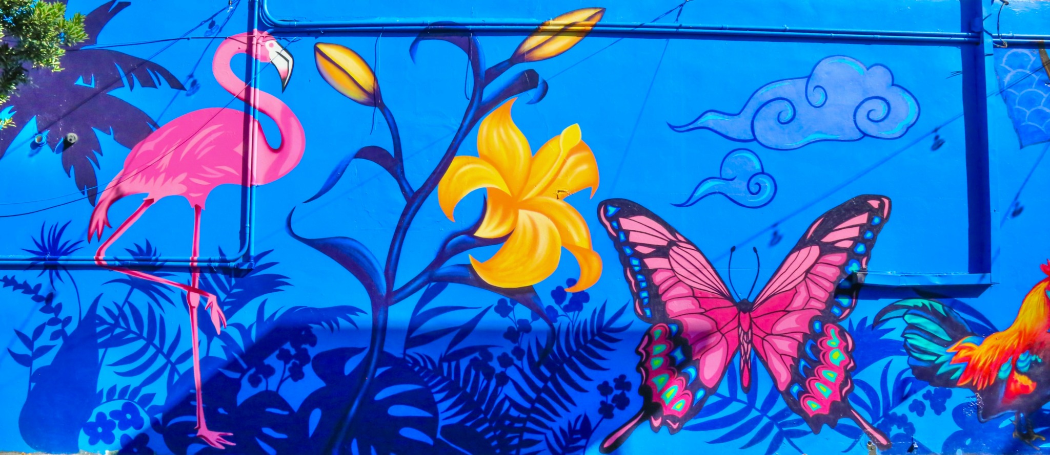 Pink flamingo, yellow lily, pink butterfly, and colorful bird on blue background with plants and clouds.