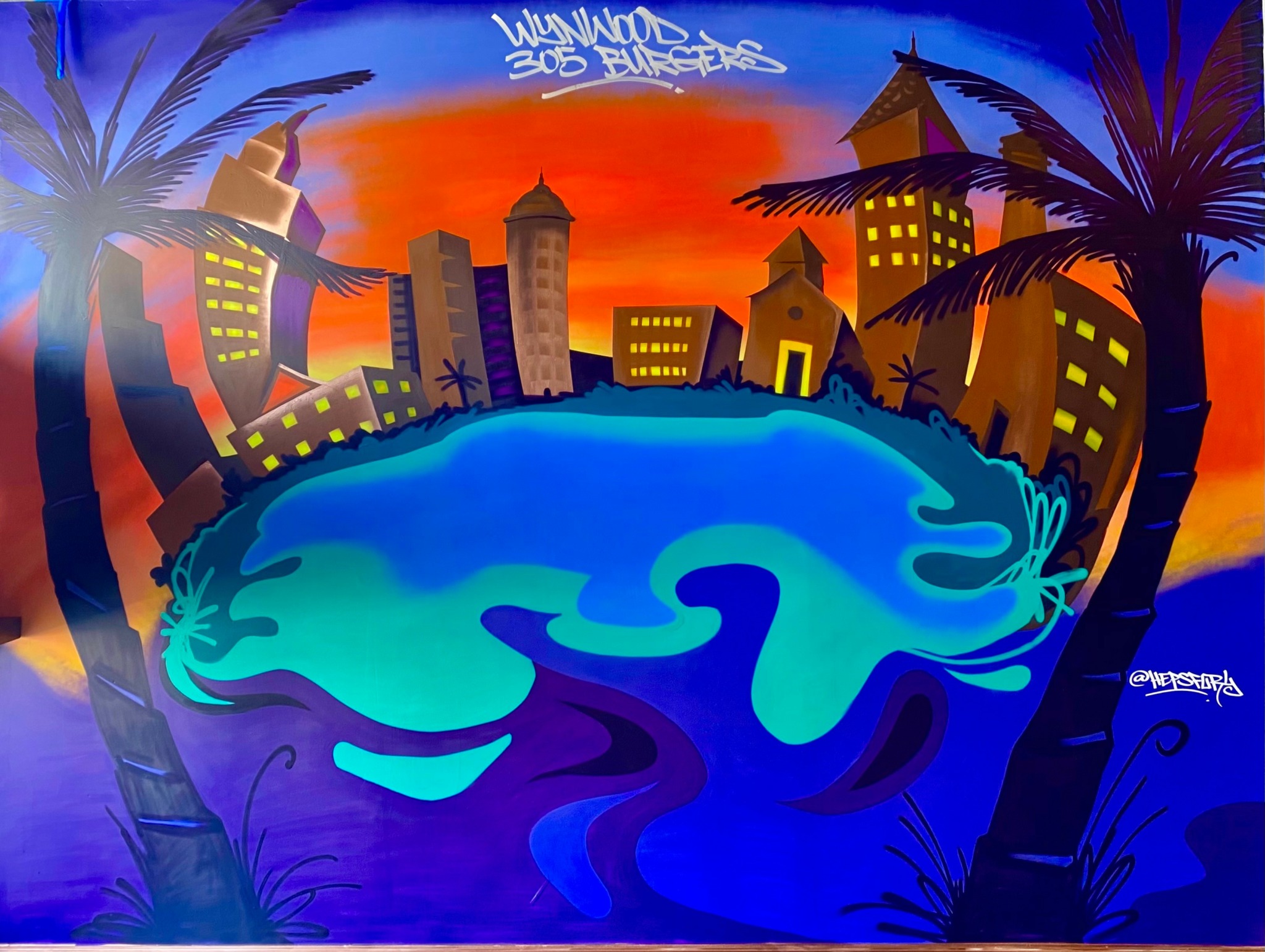City skyline with buildings, palm trees, and a large glowing blue pool in foreground at sunset.