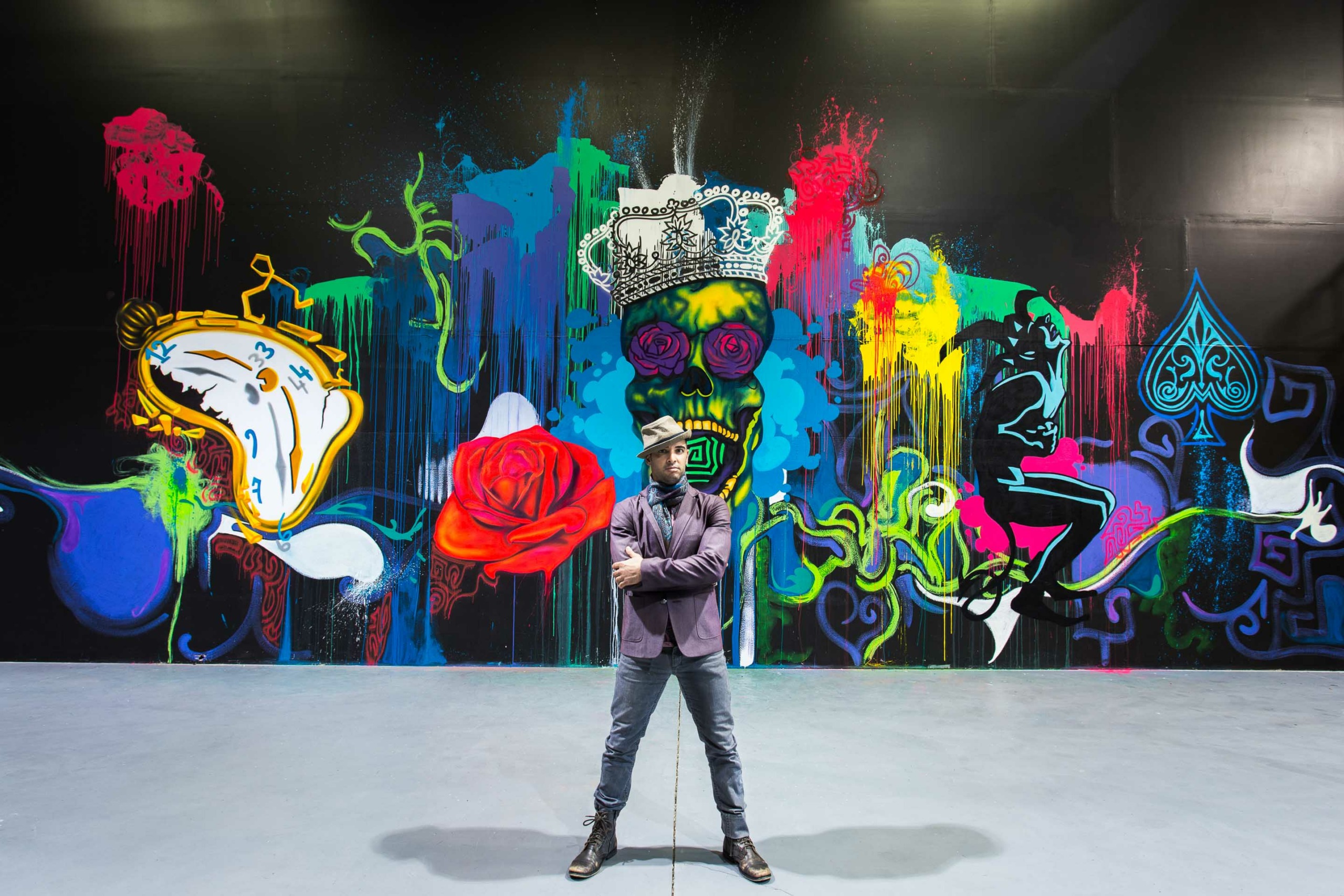 Person standing in front of a colorful graffiti mural with various abstract shapes and designs.