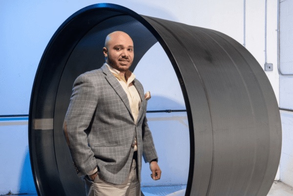 Man in a suit standing inside a large, black, circular tunnel-like structure against a blue background.