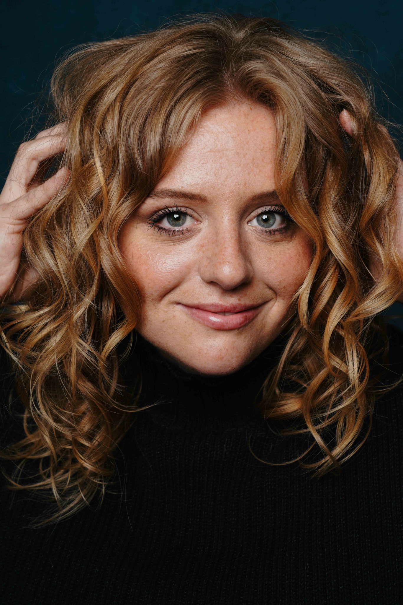 Close-up of a woman with curly hair and blue eyes smiling, wearing a black top.
