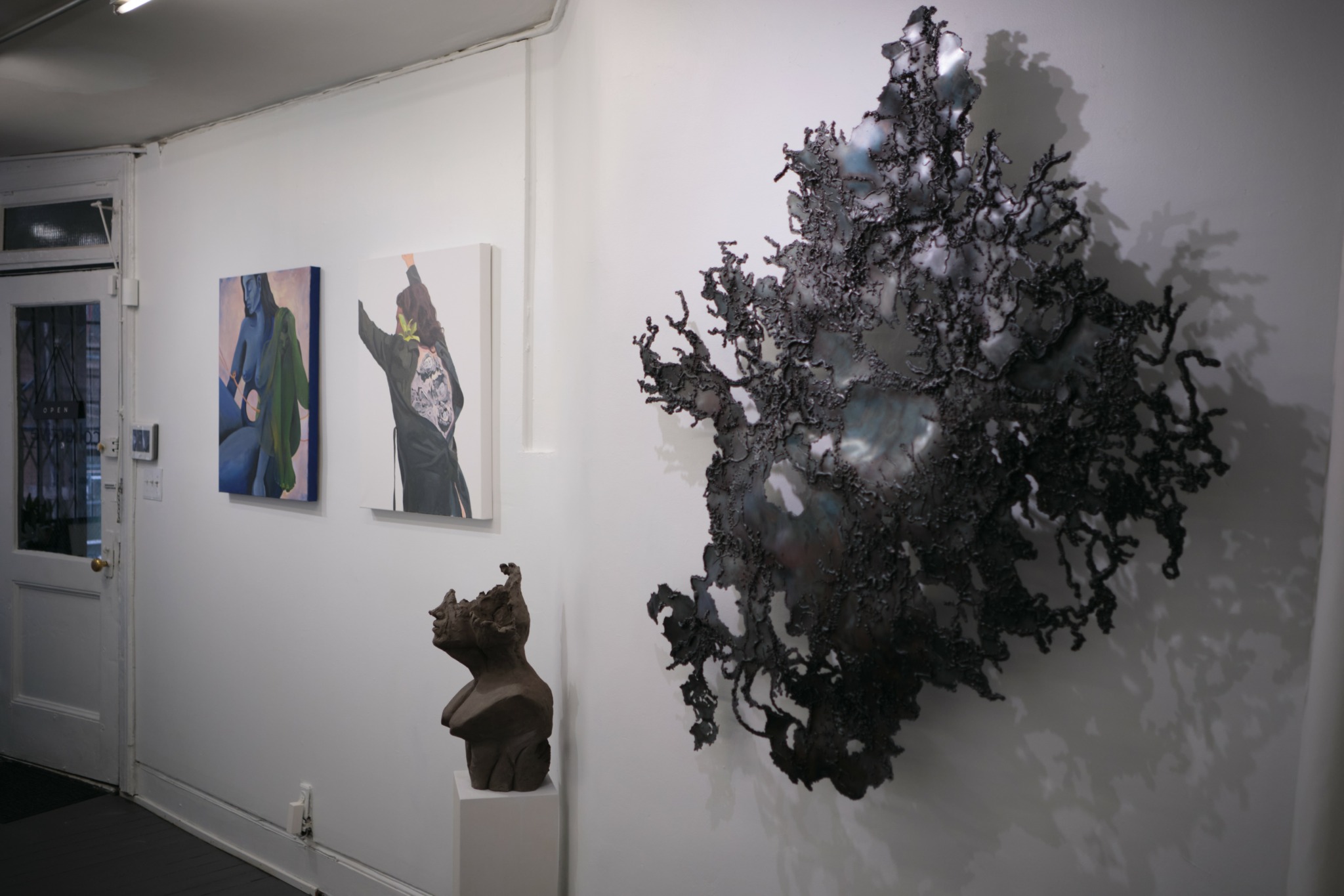 Gallery wall with two paintings and a sculpture of a dog, with a large abstract tree sculpture on the right.