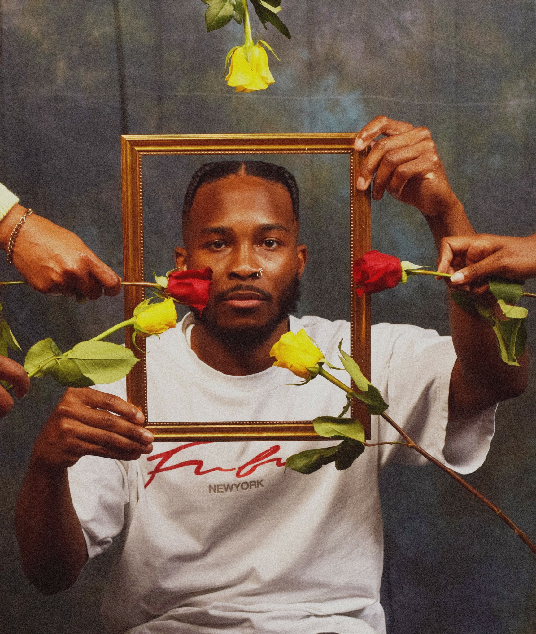 Person holding a picture frame with flowers around their face, against a dark background.