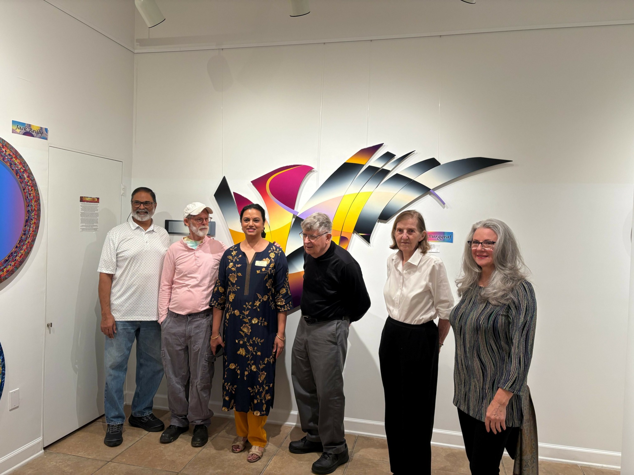 Six people stand in front of colorful abstract wall art in an art gallery, smiling for the photo.