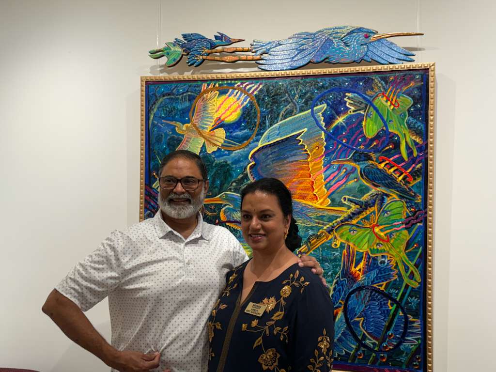 Two people standing in front of a colorful abstract painting, smiling at the camera.