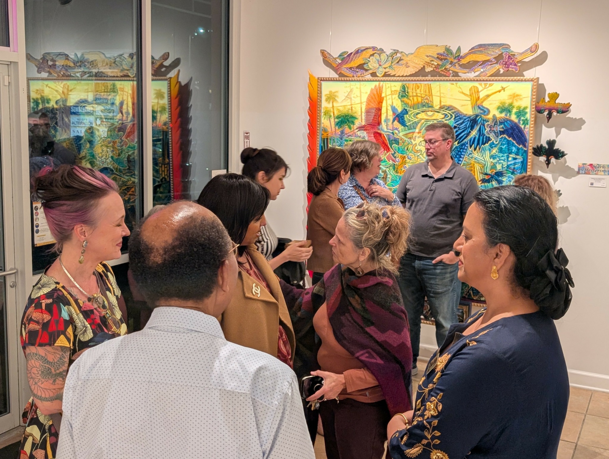 Group of people gathered in an art gallery, looking at colorful paintings on the wall.