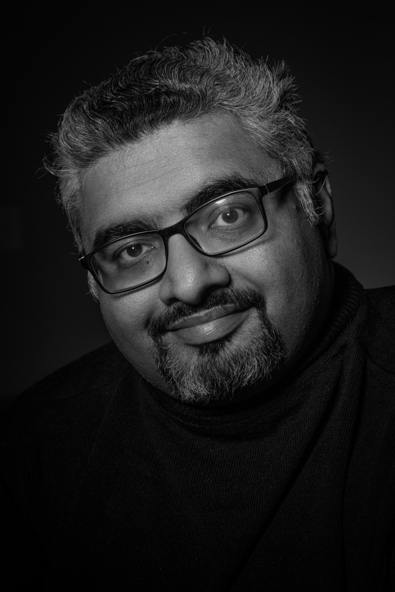 Portrait of a man with glasses, short curly hair, and a beard, smiling at the camera.