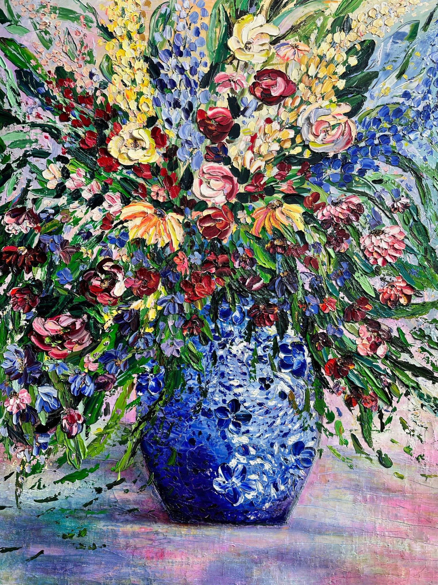 Colorful floral bouquet in a blue patterned vase with pink, yellow, and purple flowers and green leaves.