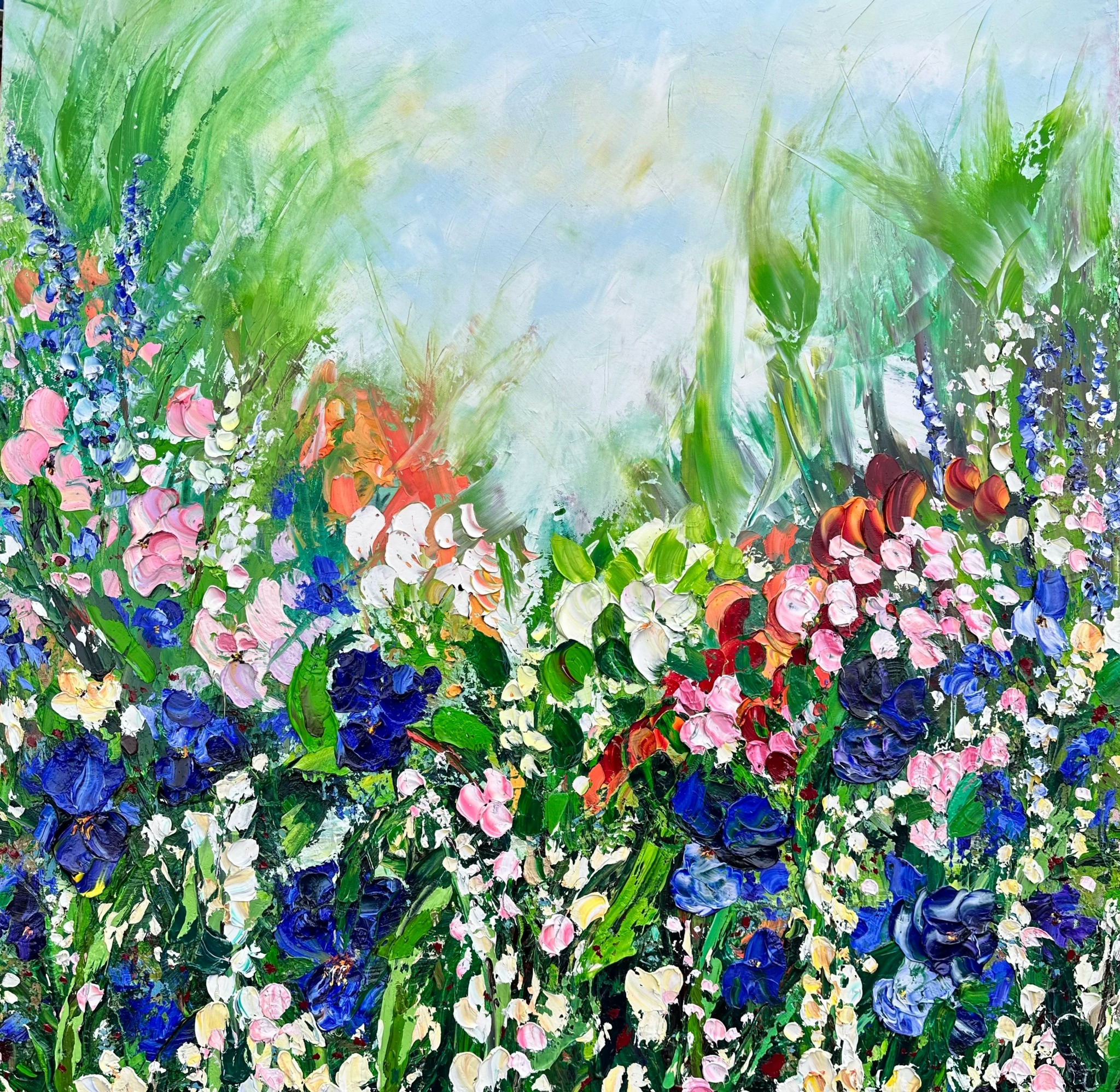 Colorful garden with various flowers and green foliage, bright sky background.