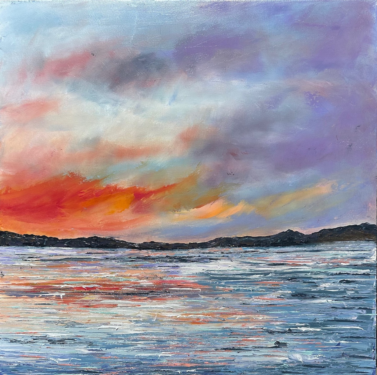 Colorful sky with orange, pink, purple, and blue clouds over a body of water with distant land.