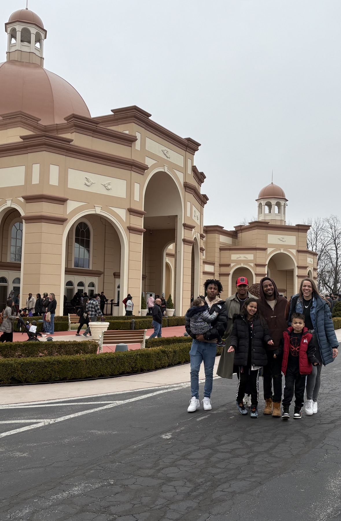Group of people standing on street in front of a large, ornate building with domes and arches.