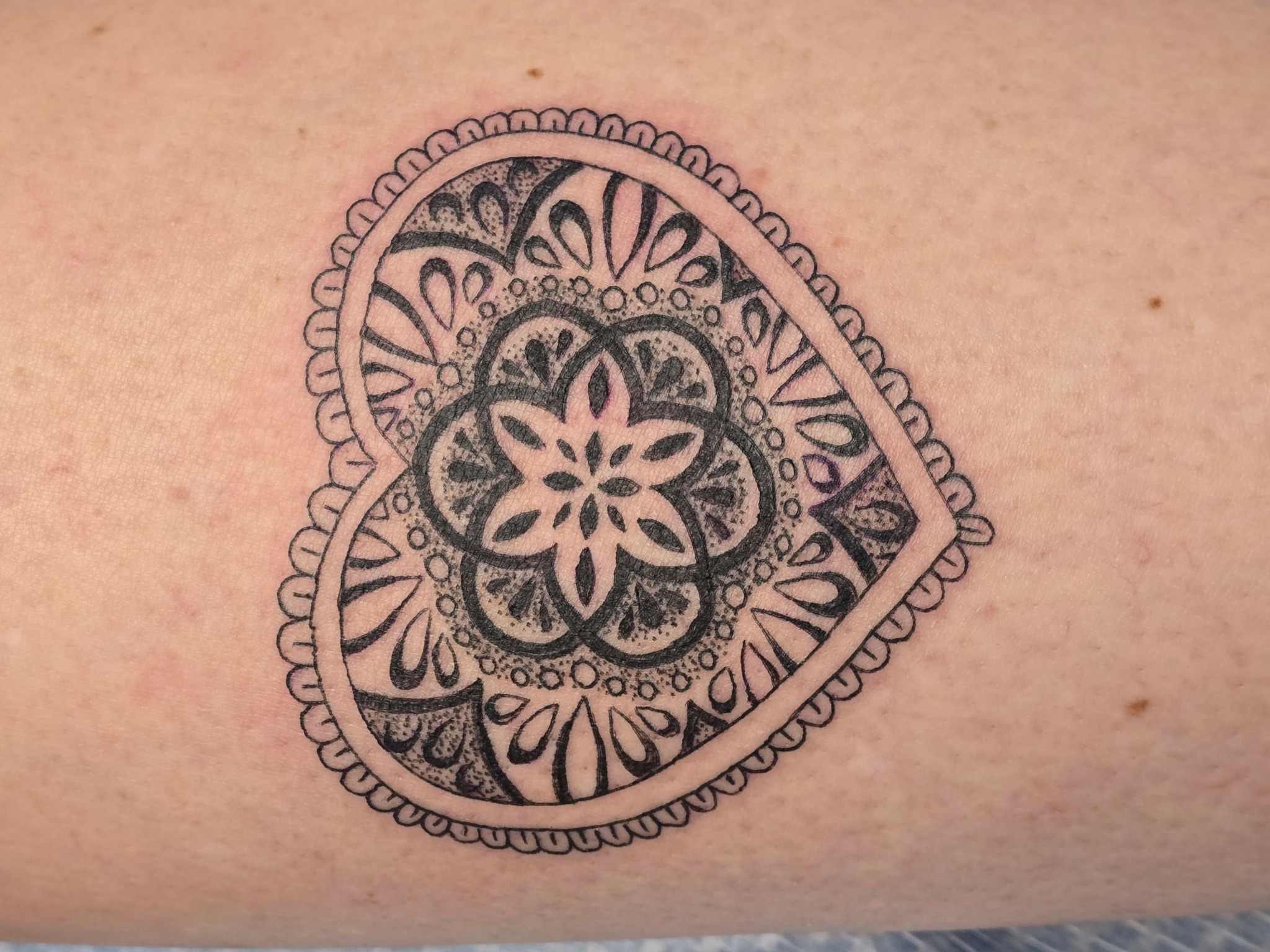 Heart-shaped tattoo with intricate floral and geometric patterns inside, outlined with a decorative border.