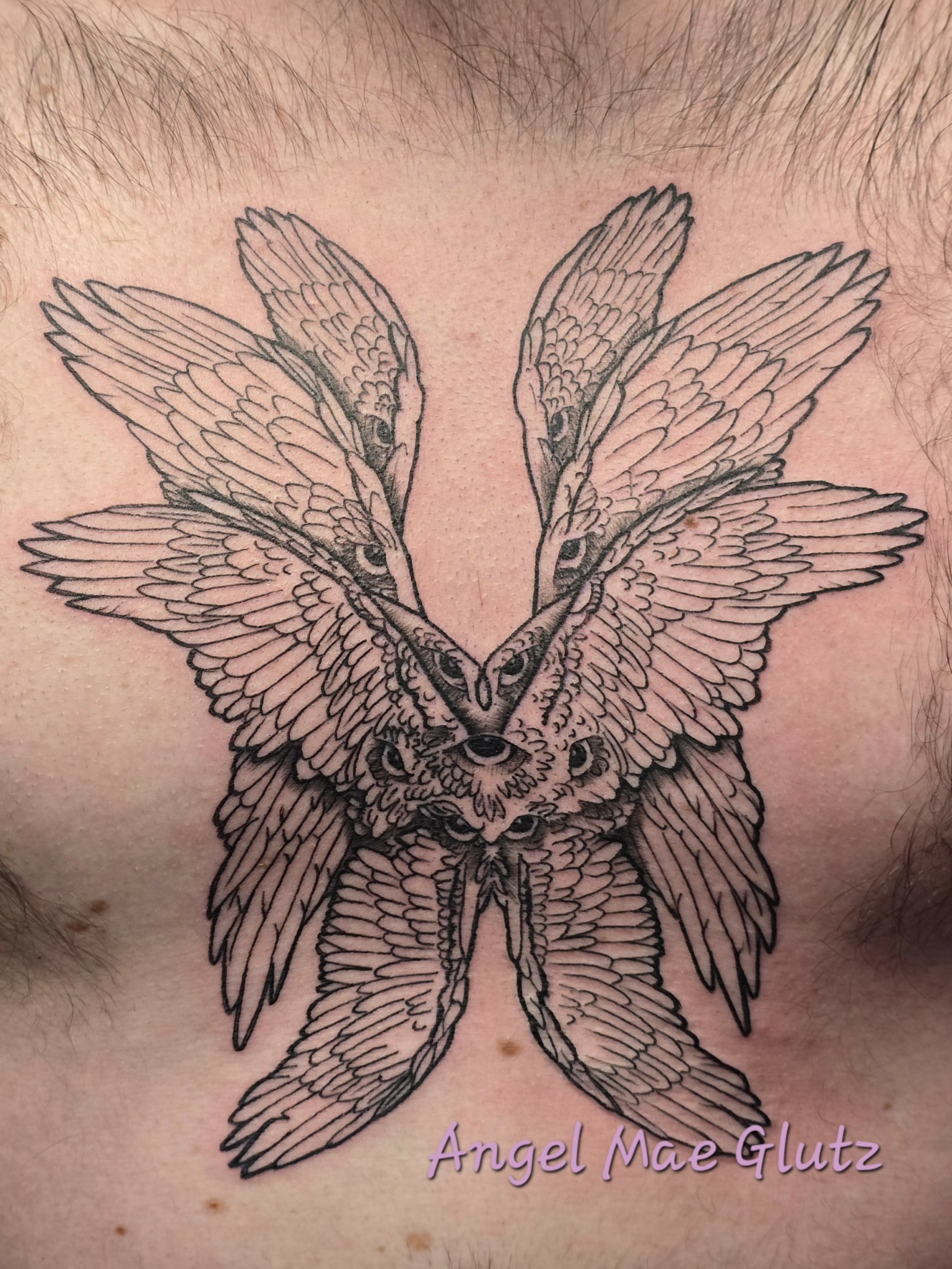 Tattoo of a symmetrical owl with wings and feathers extending outward, detailed line work, on skin.