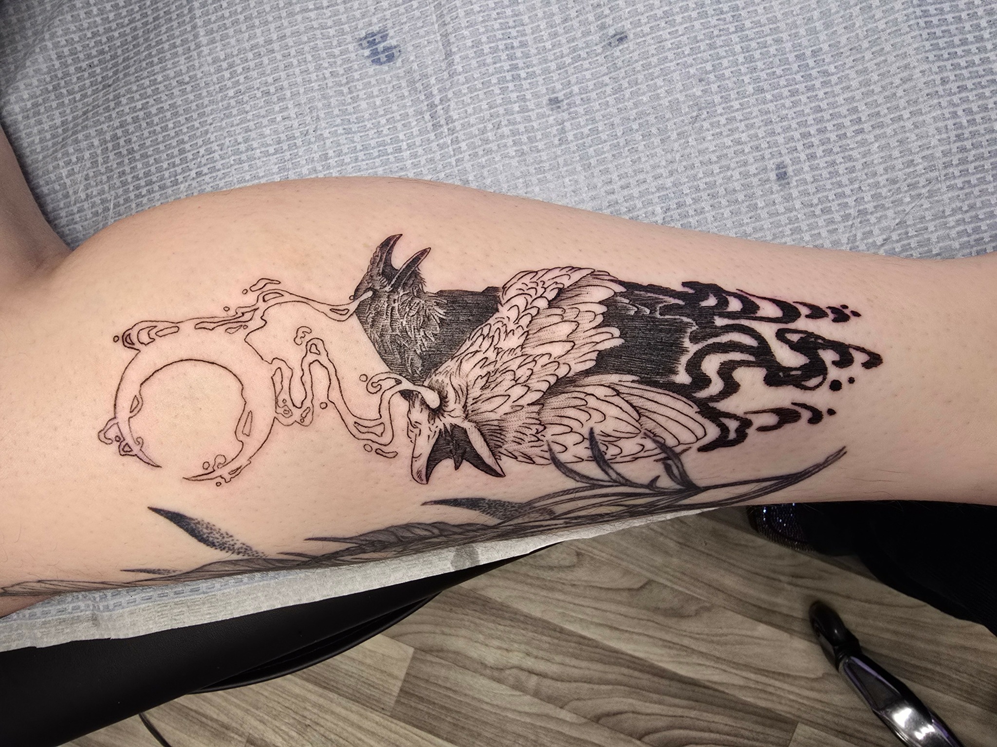 Tattoo of a wolf with wings, surrounded by flames and a circular design, on a person's arm.