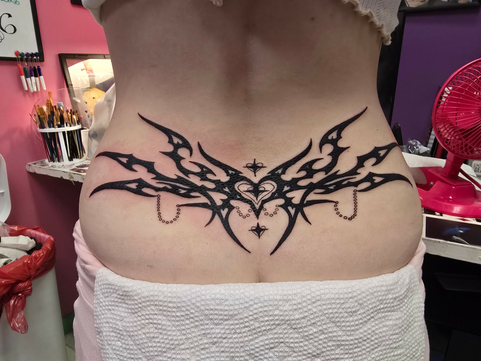 Black tribal-style tattoo across lower abdomen with symmetrical design and heart shape in the center.