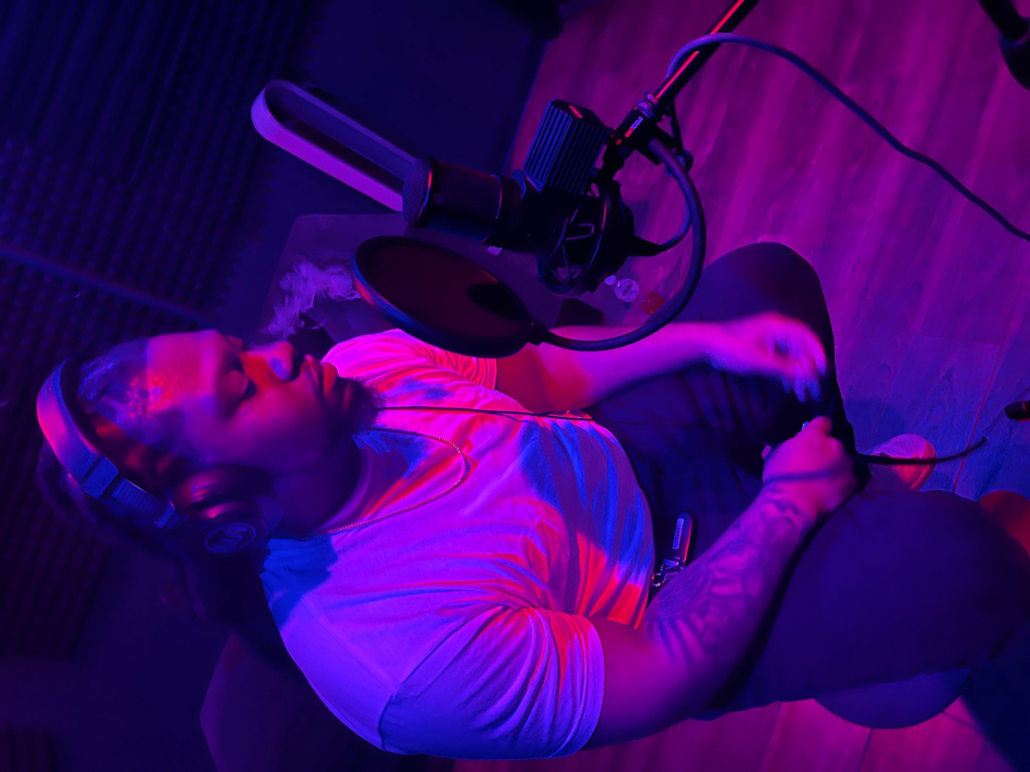 Person lying on floor with microphone and purple lighting, wearing a striped cap and white shirt.