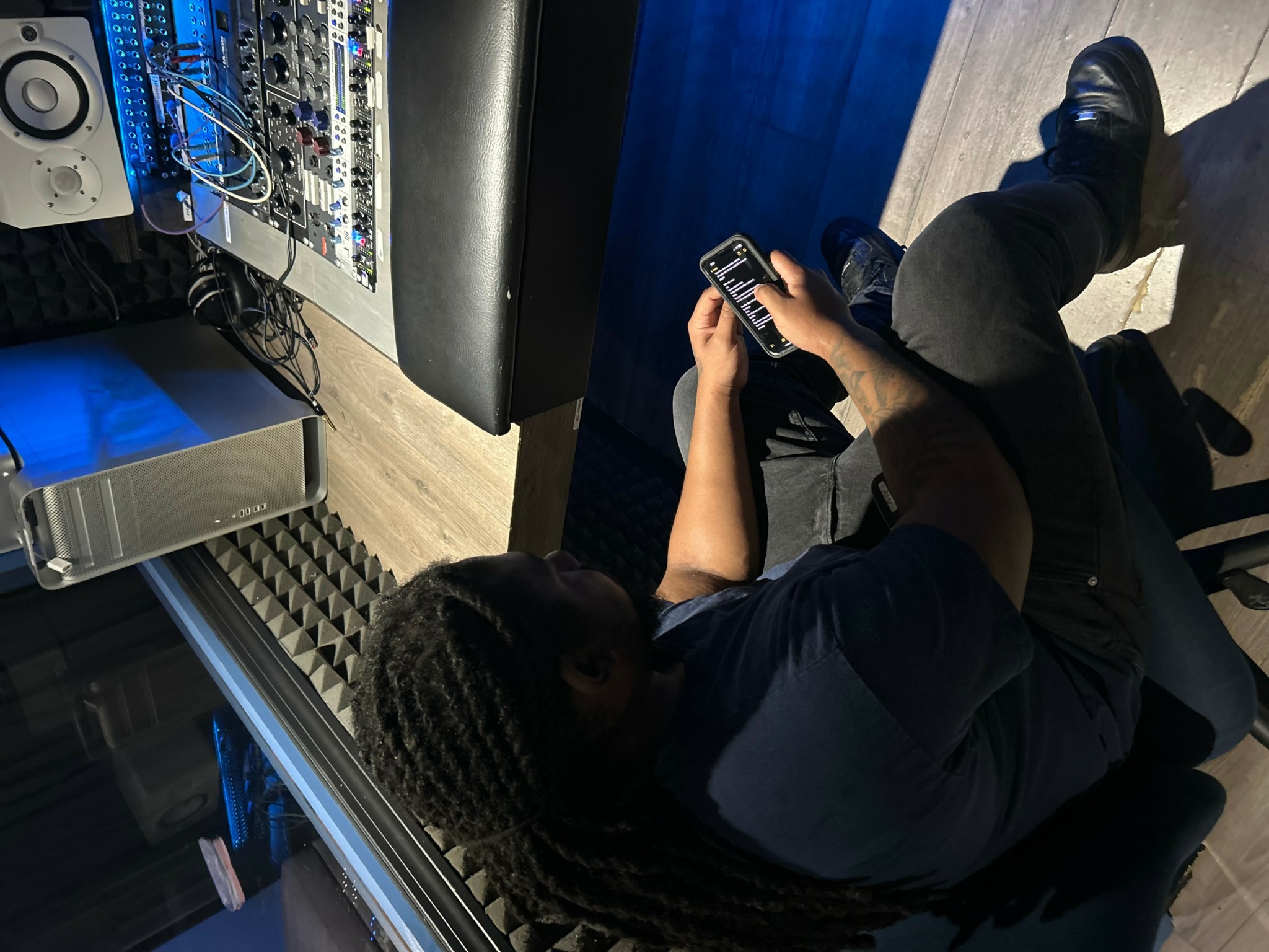 Child sitting on the floor using a remote control, with electronic equipment nearby and a blue wall.