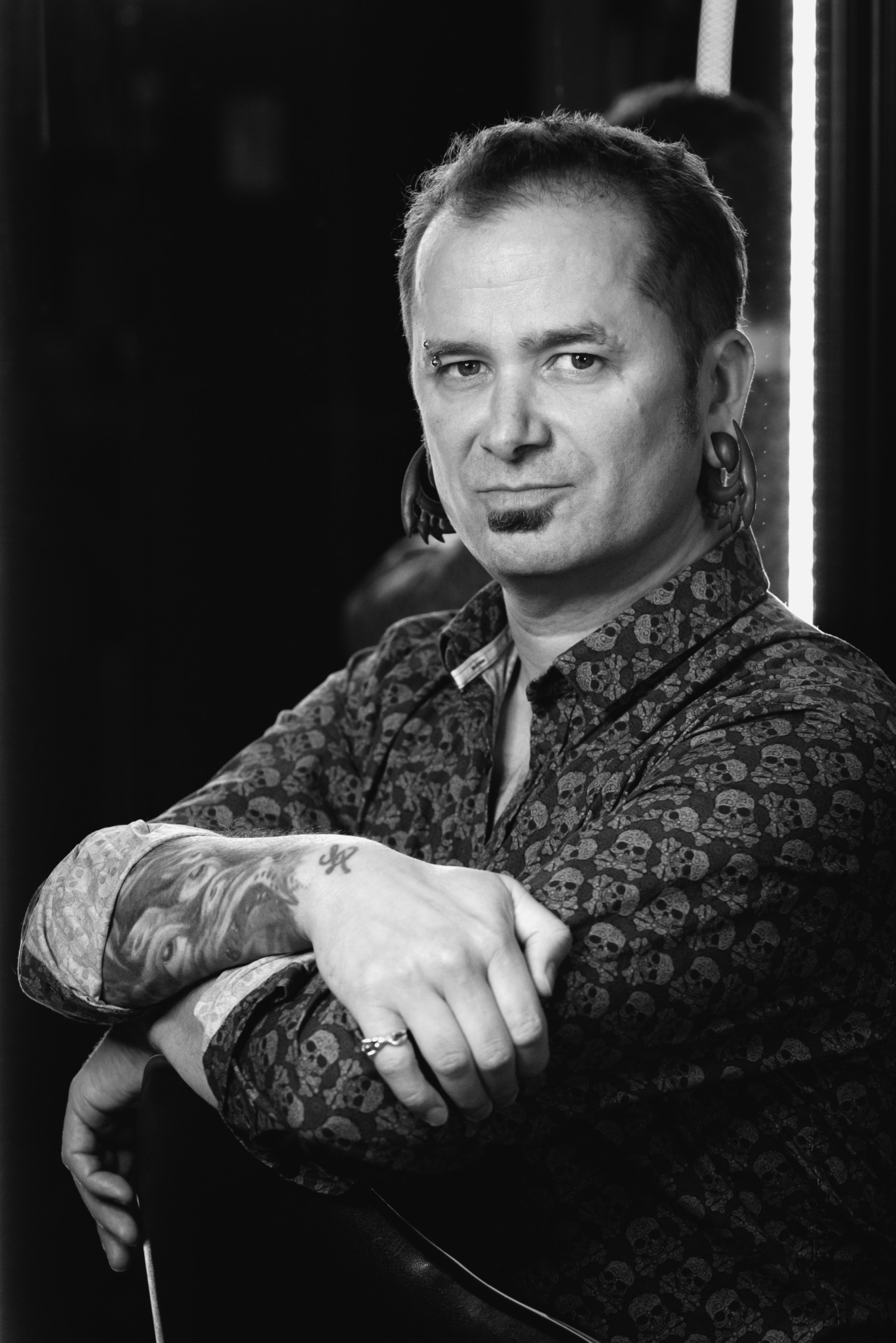 Man with short hair and patterned shirt, arms crossed, in black and white photo.