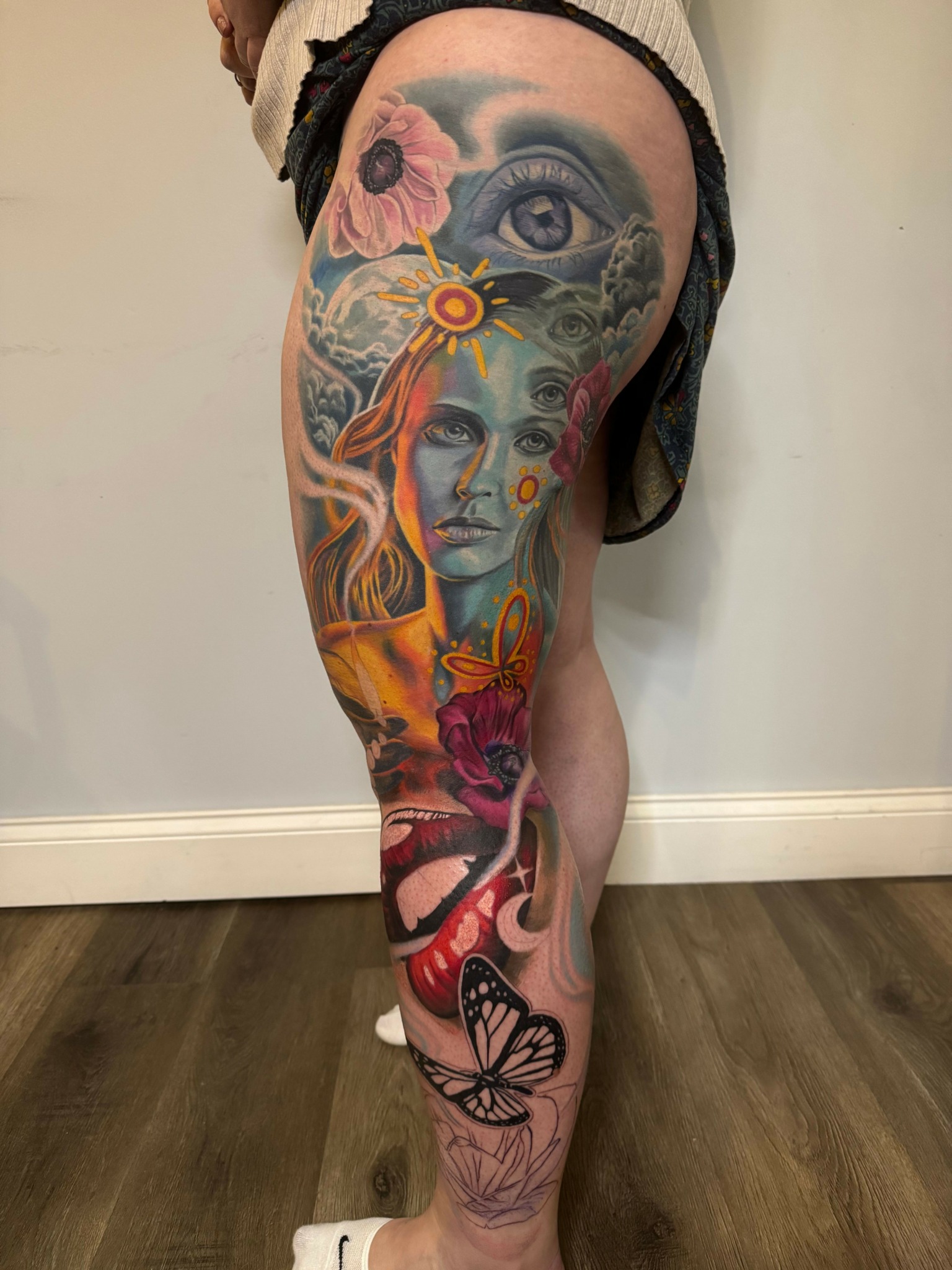 Arm tattoo featuring a woman's face, flowers, a butterfly, and colorful abstract elements.