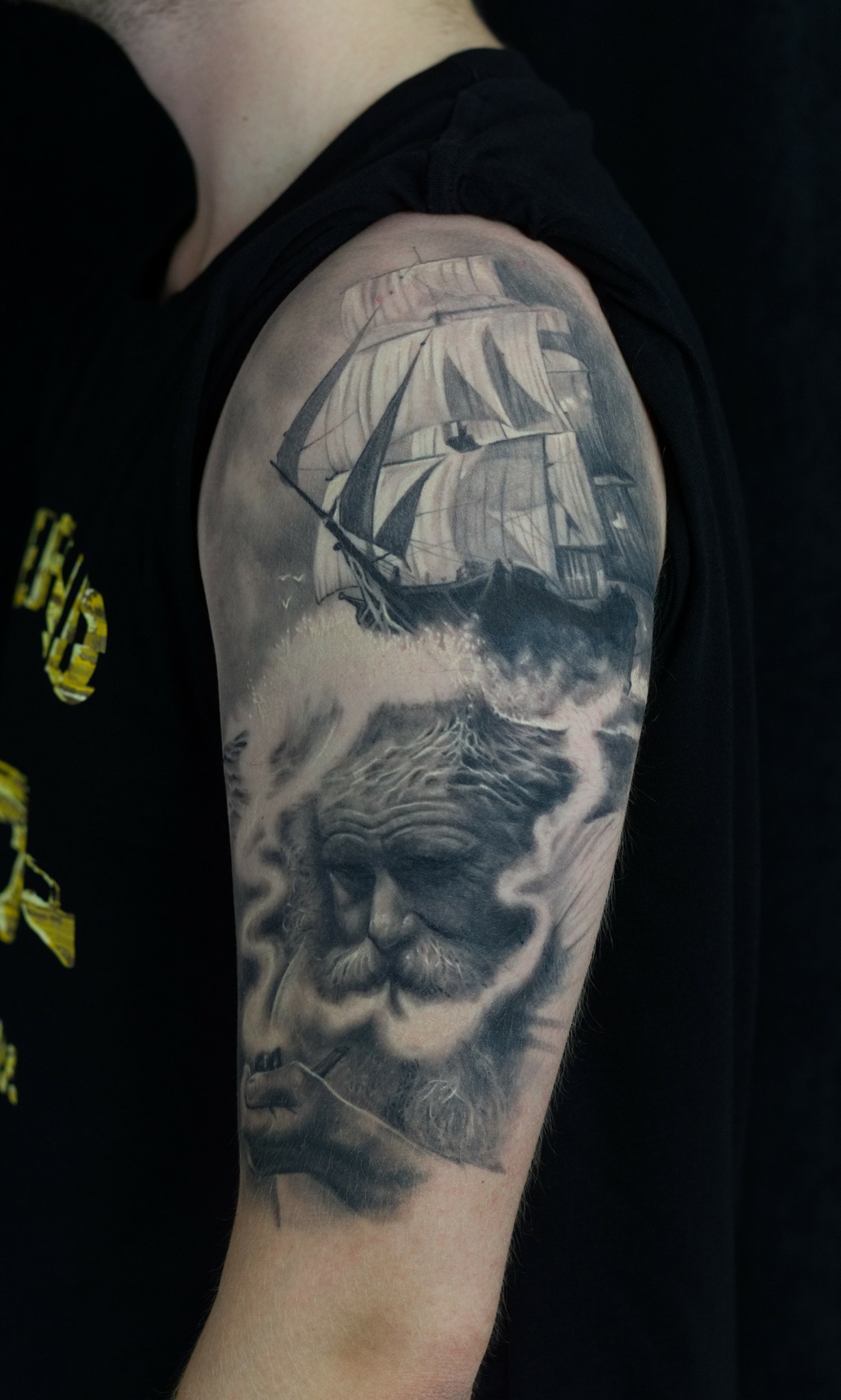 Tattoo of a sailing ship, waves, and an old man's face on upper arm.