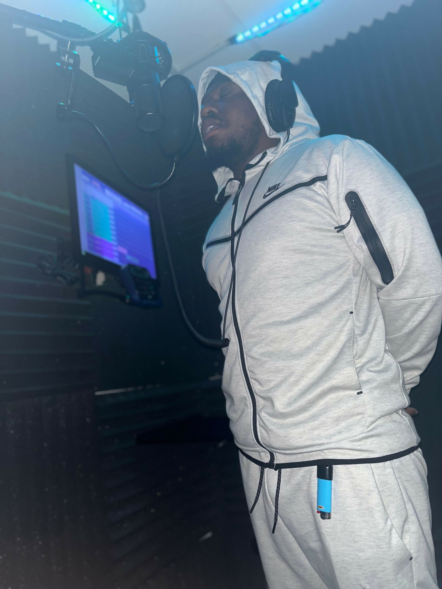Person wearing a white hoodie and sweatpants, standing in a DJ booth with equipment and a monitor.