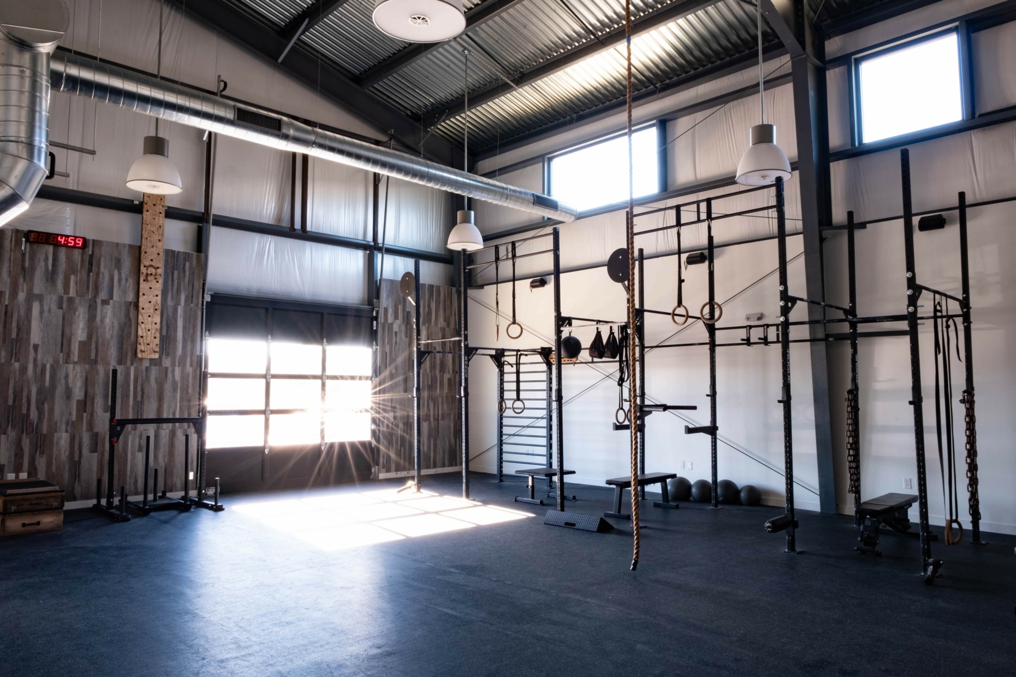 Indoor gym with black metal climbing structures, wooden wall panels, and large windows letting in natural light.
