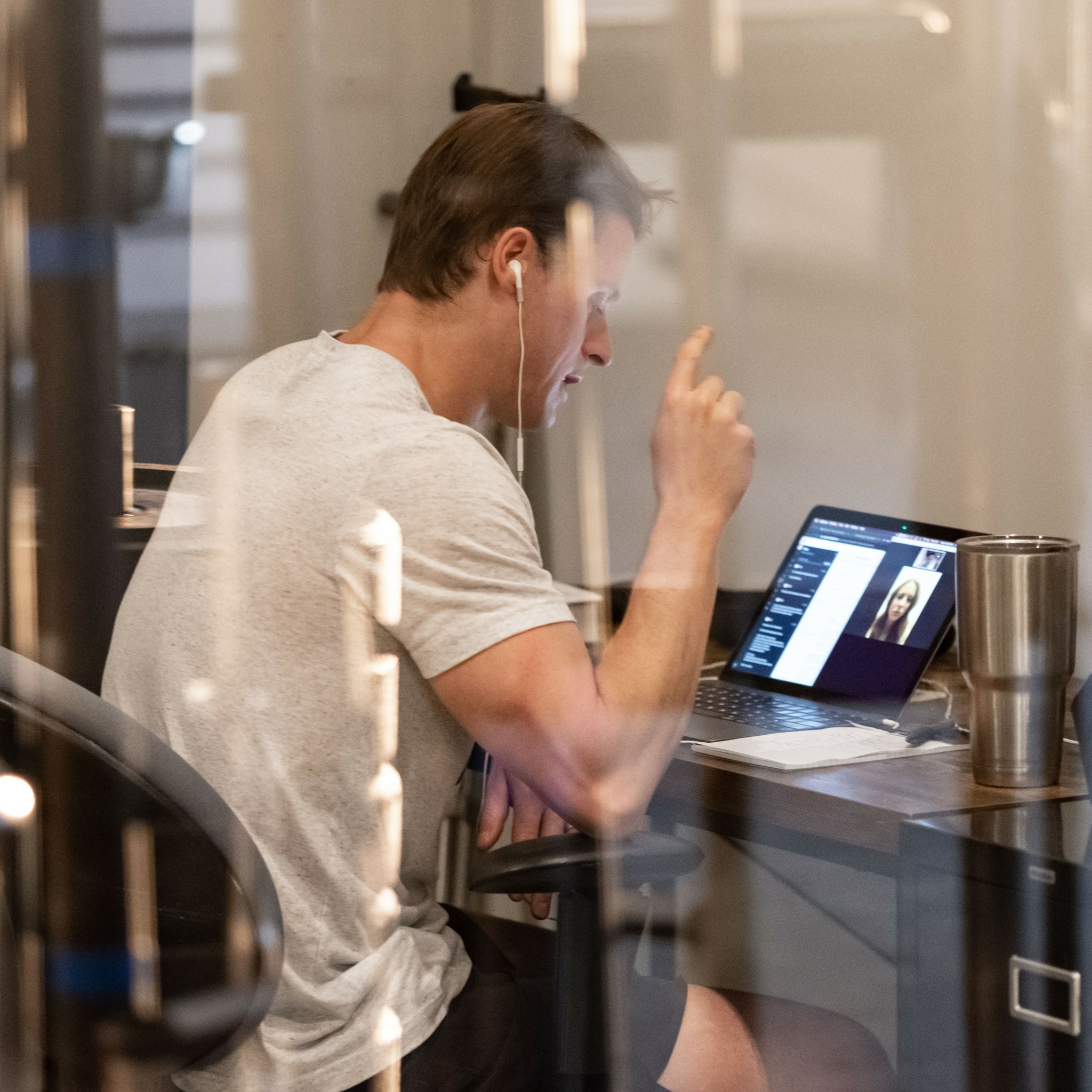 Person with short hair, wearing a light-colored shirt, sitting at a desk, pointing upward, using a tablet device.