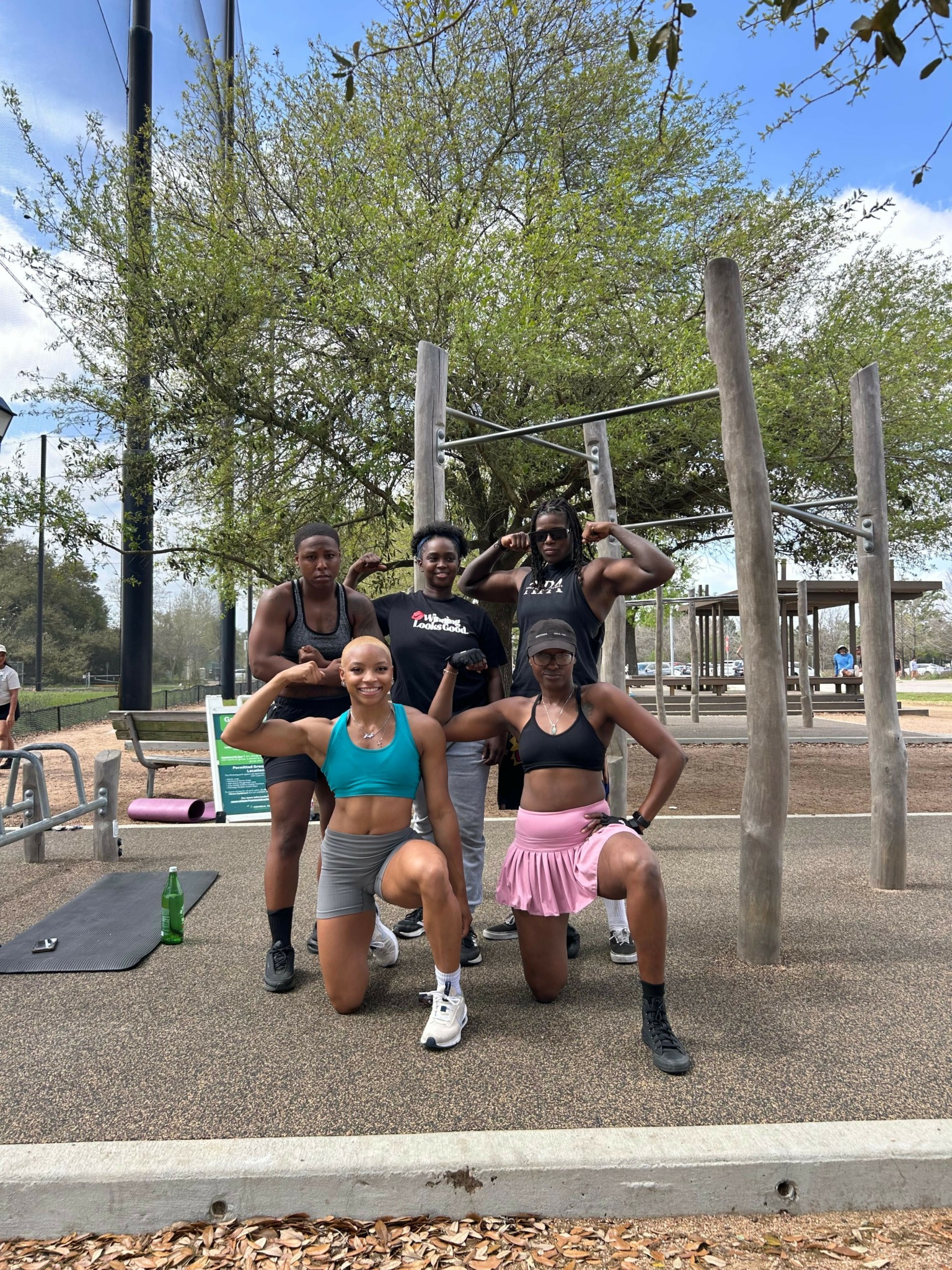 Group of people exercising outdoors on a paved path with trees and a swing set in the background.