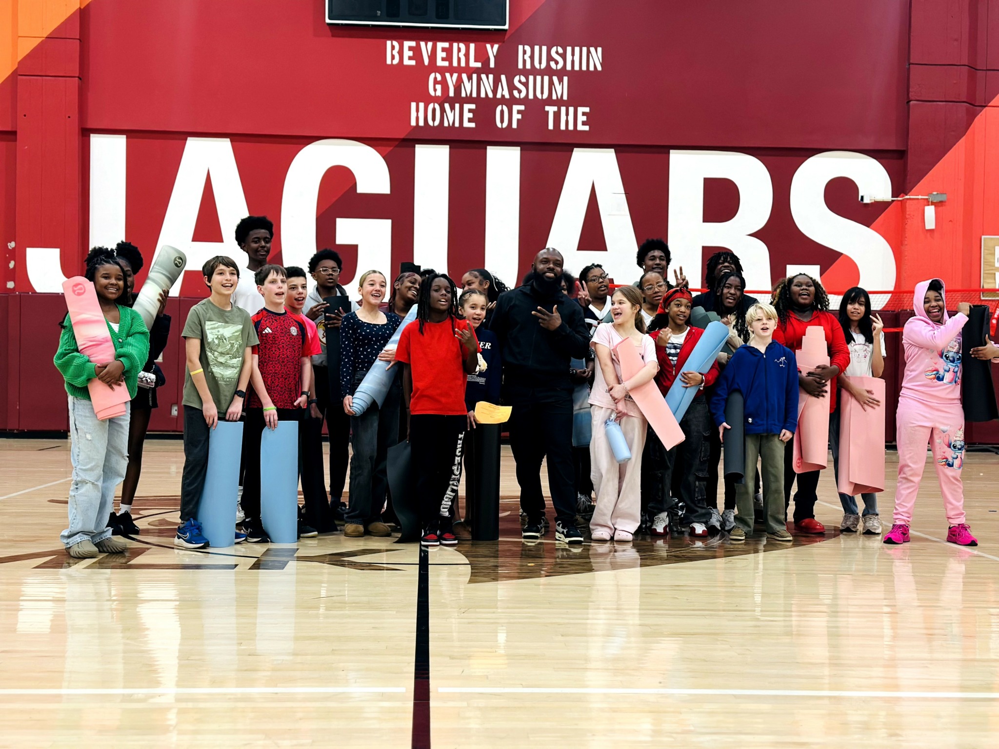 Group of children and adults standing in a gymnasium in front of a large 'Jaguars' sign.