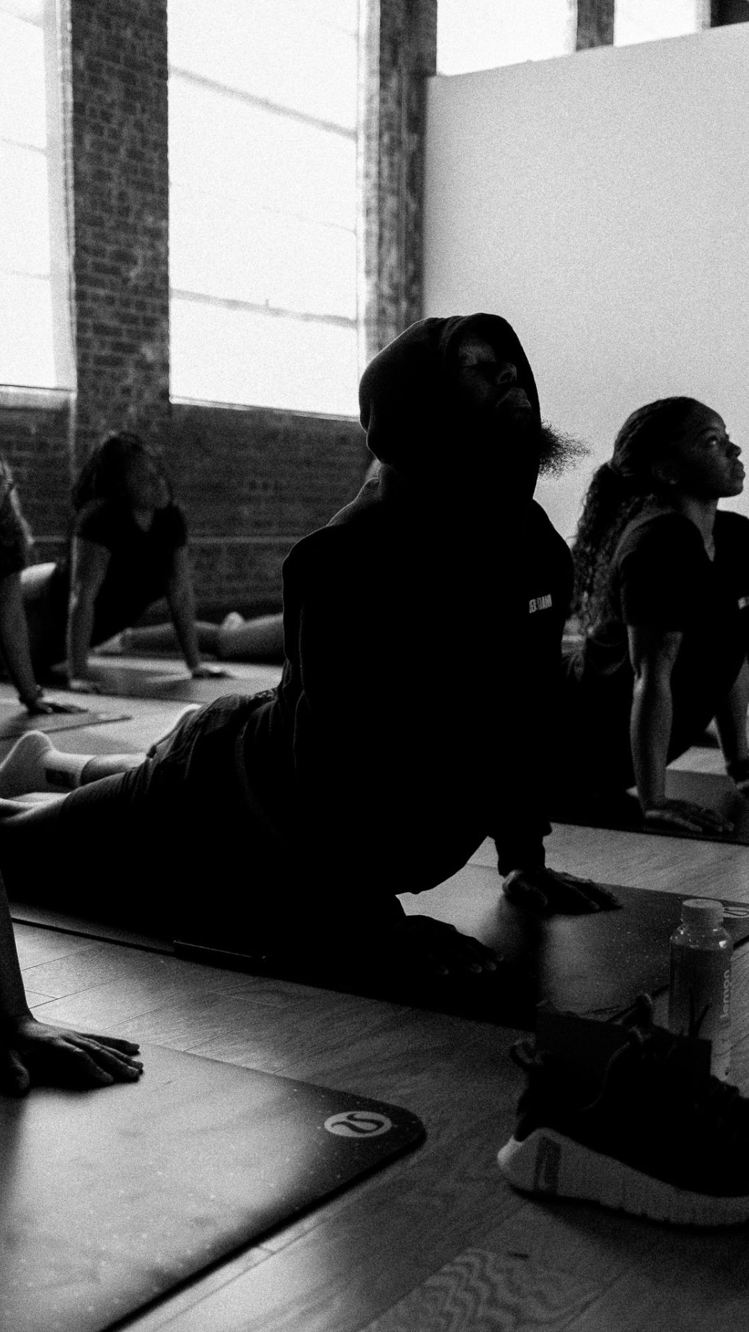 People practicing yoga in a studio with large windows and brick walls, some in cobra pose.