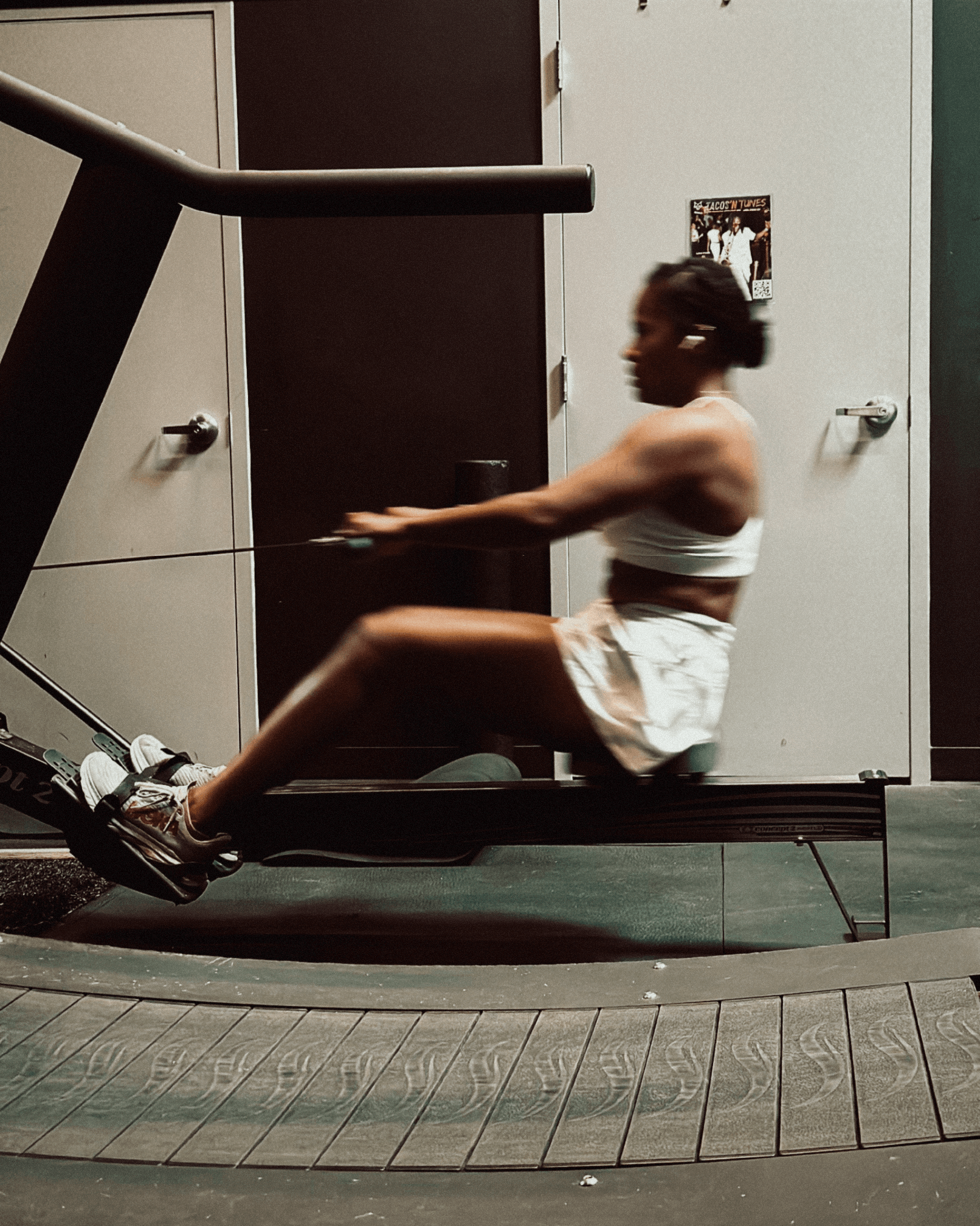 Person using a rowing machine in a room with cabinets and a poster on the wall.